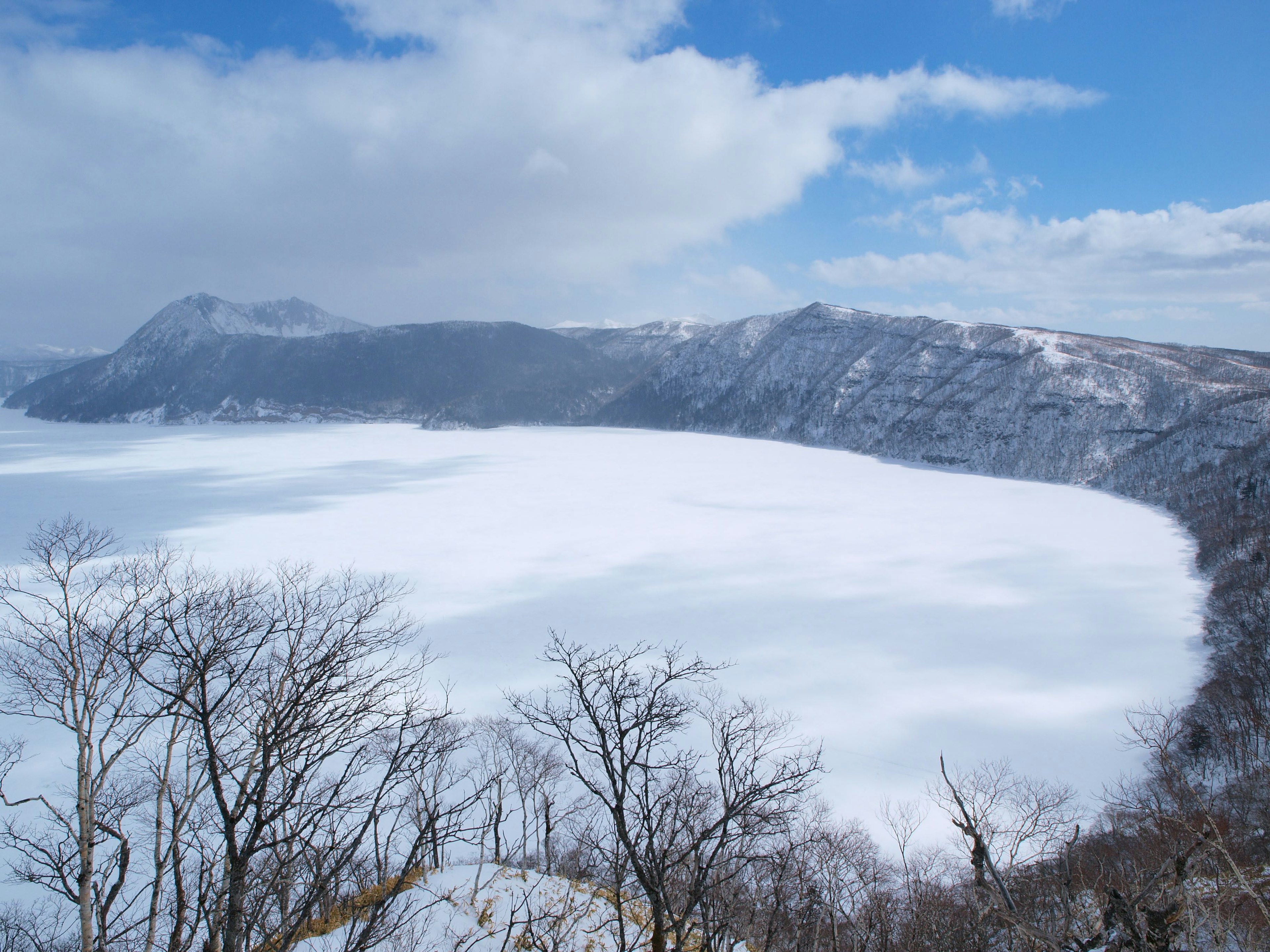 Lago coperto di neve con montagne sullo sfondo e cielo blu