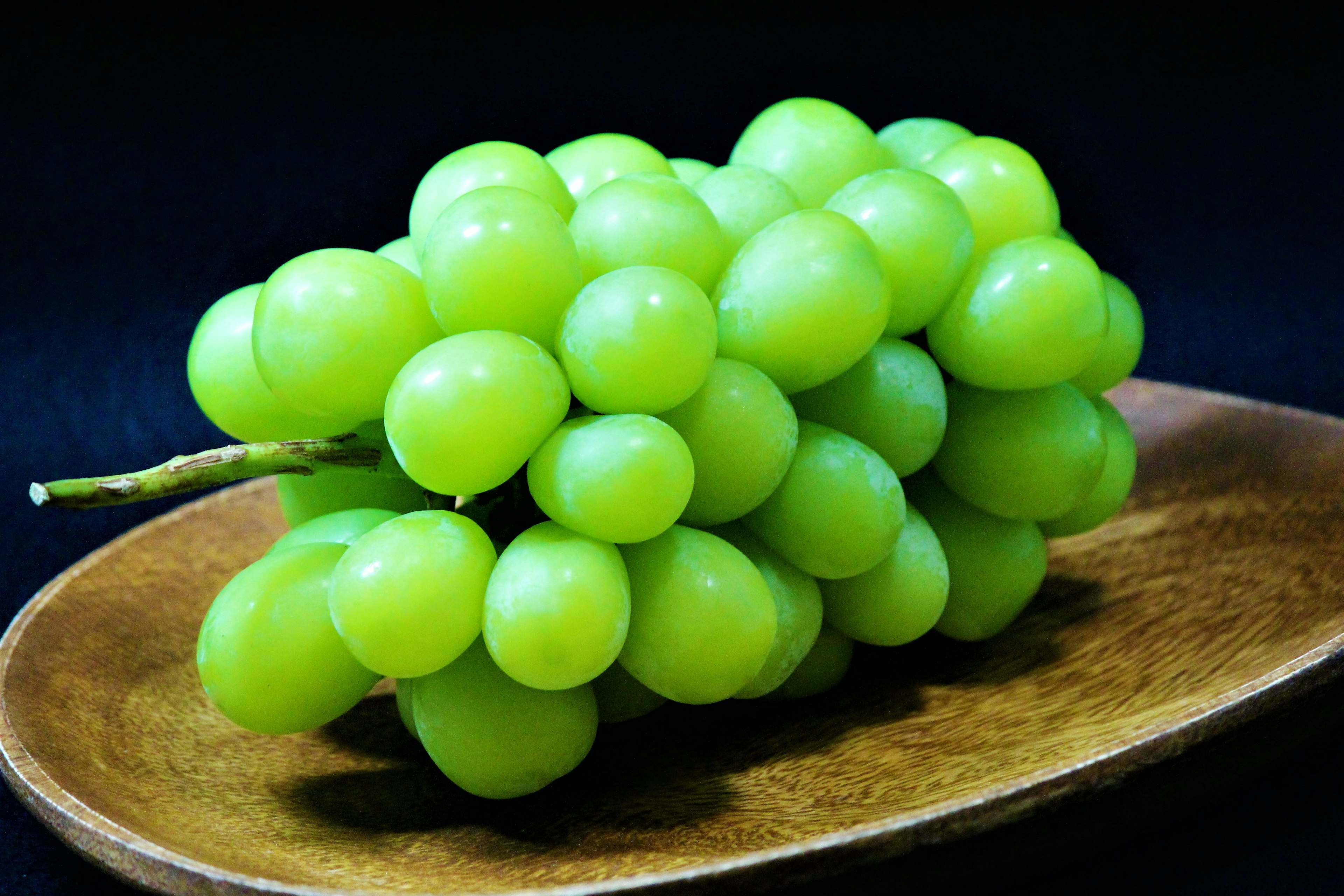 Une grappe de raisins verts sur une assiette en bois