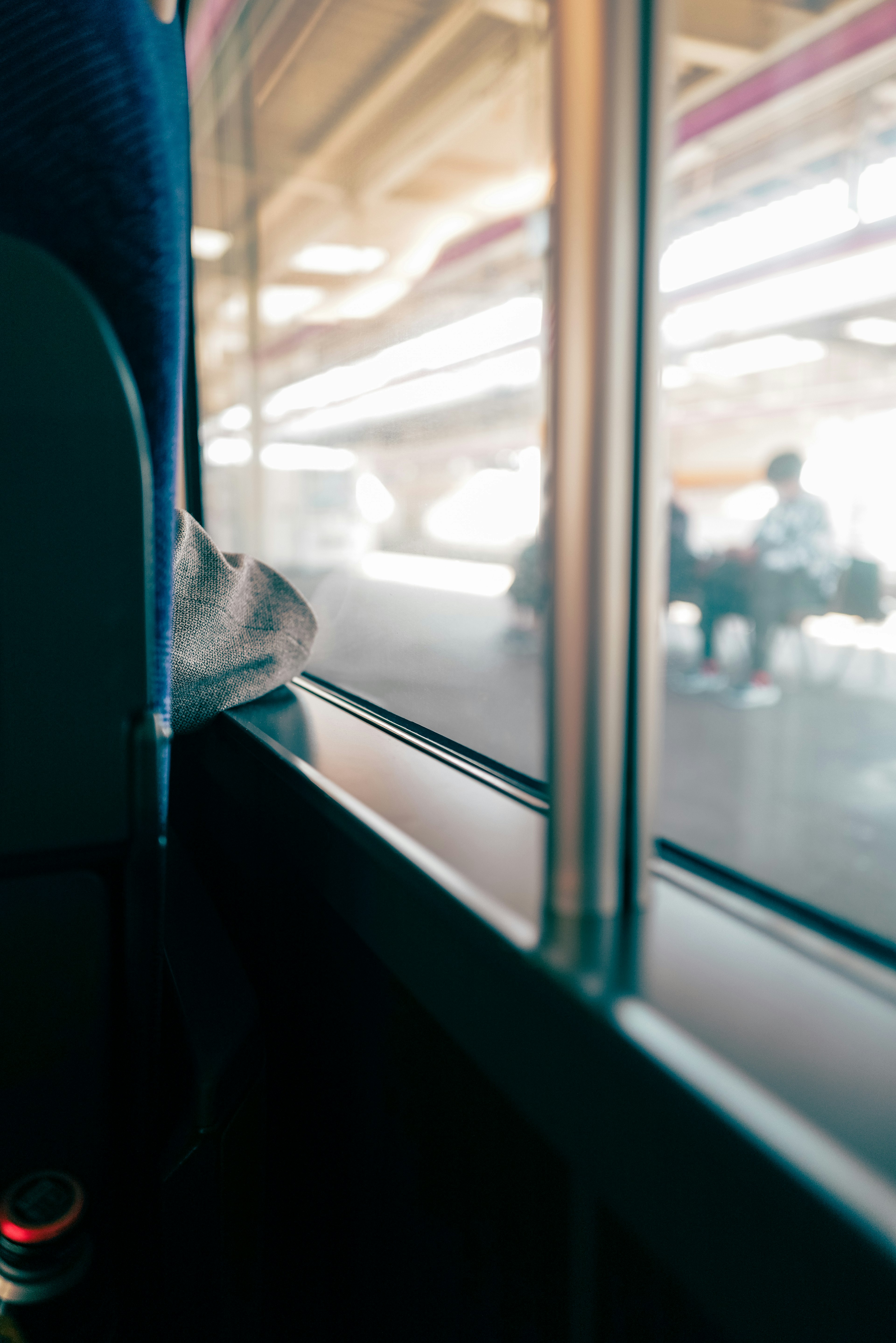 Interior bus menunjukkan kaki seseorang bersandar di ambang jendela dengan pemandangan stasiun di luar yang buram