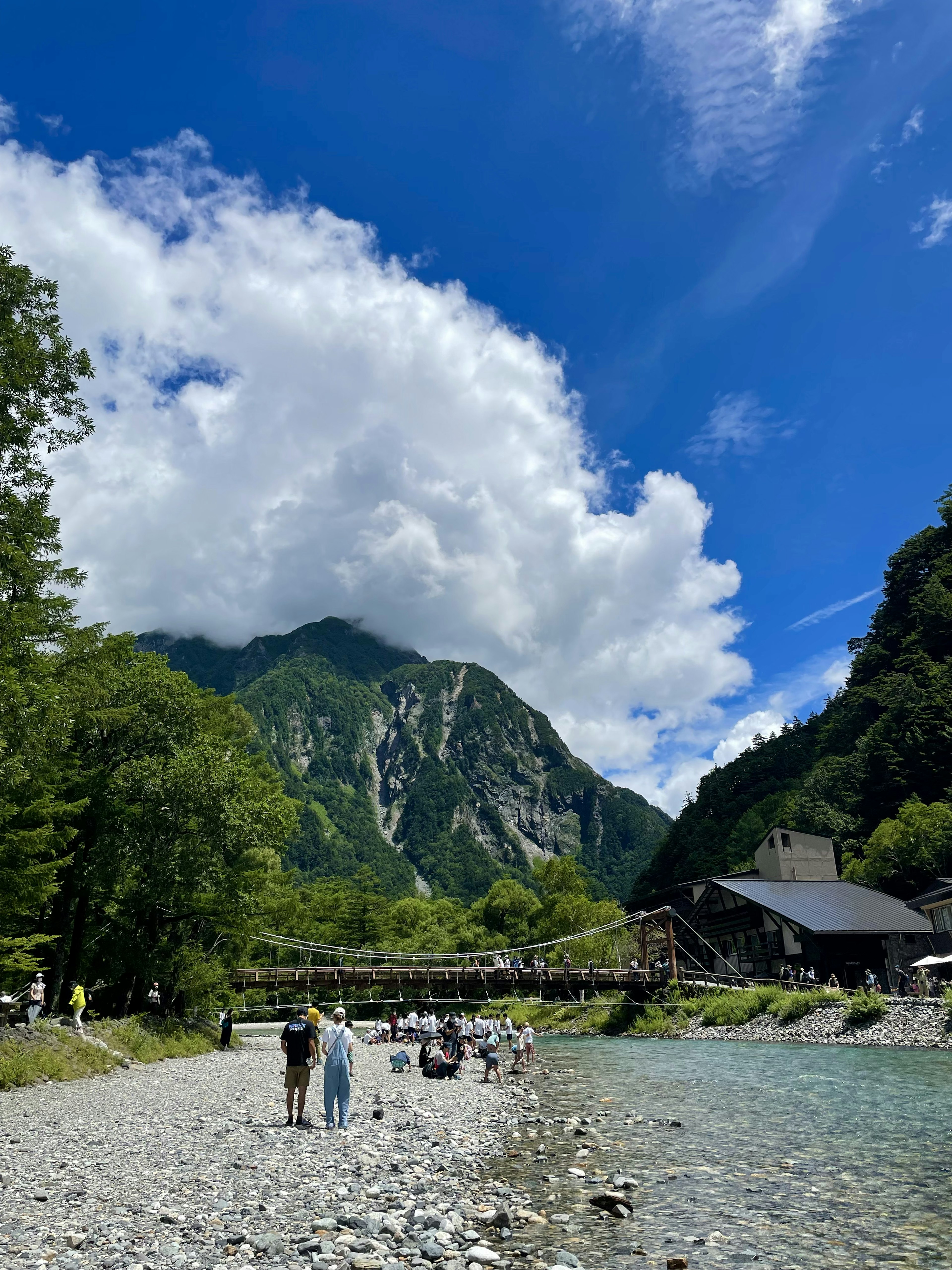 Paisaje montañoso pintoresco con cielo azul y nubes a lo largo de un río con personas caminando