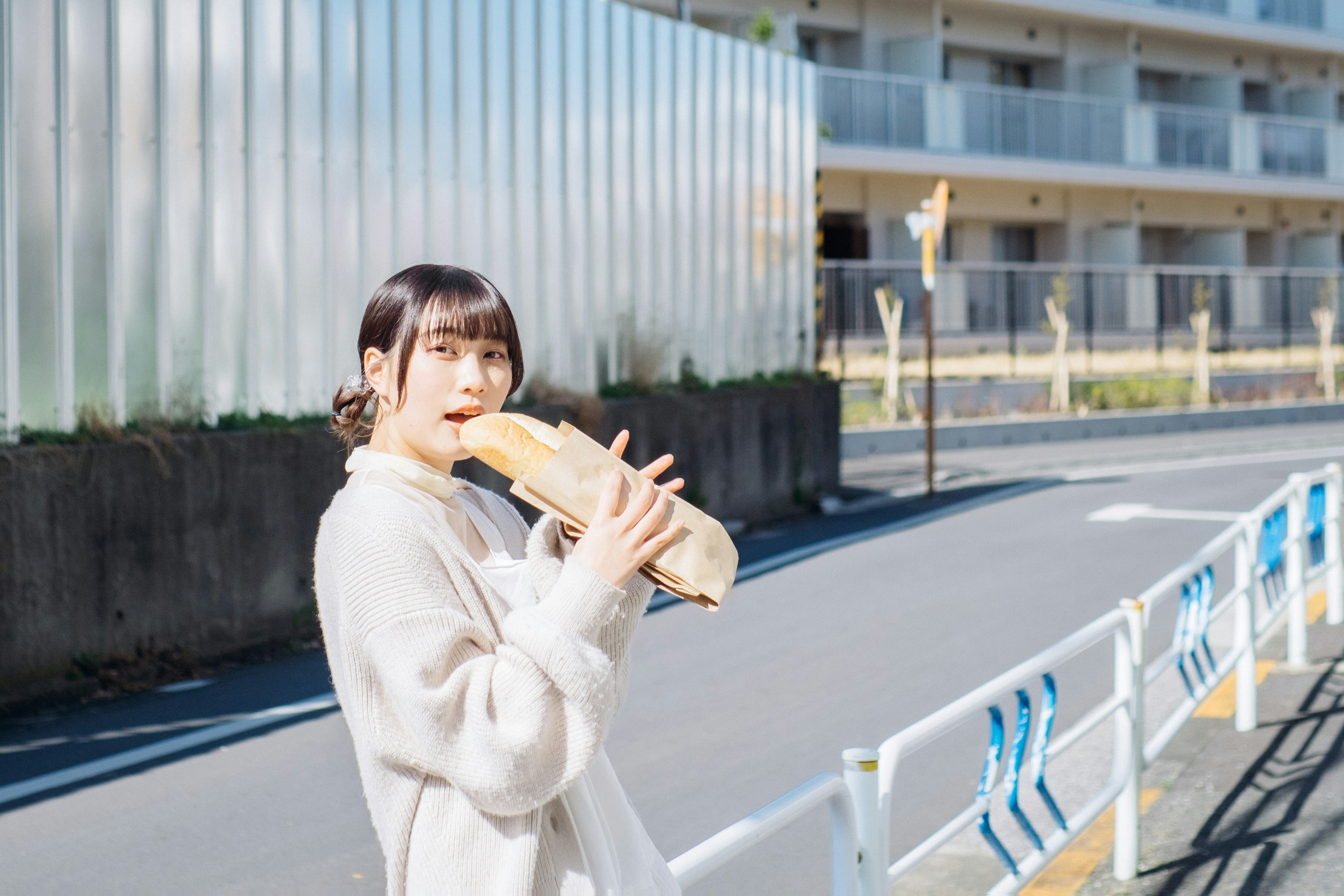 Giovane donna che tiene una baguette come se fosse uno strumento musicale in una strada della città