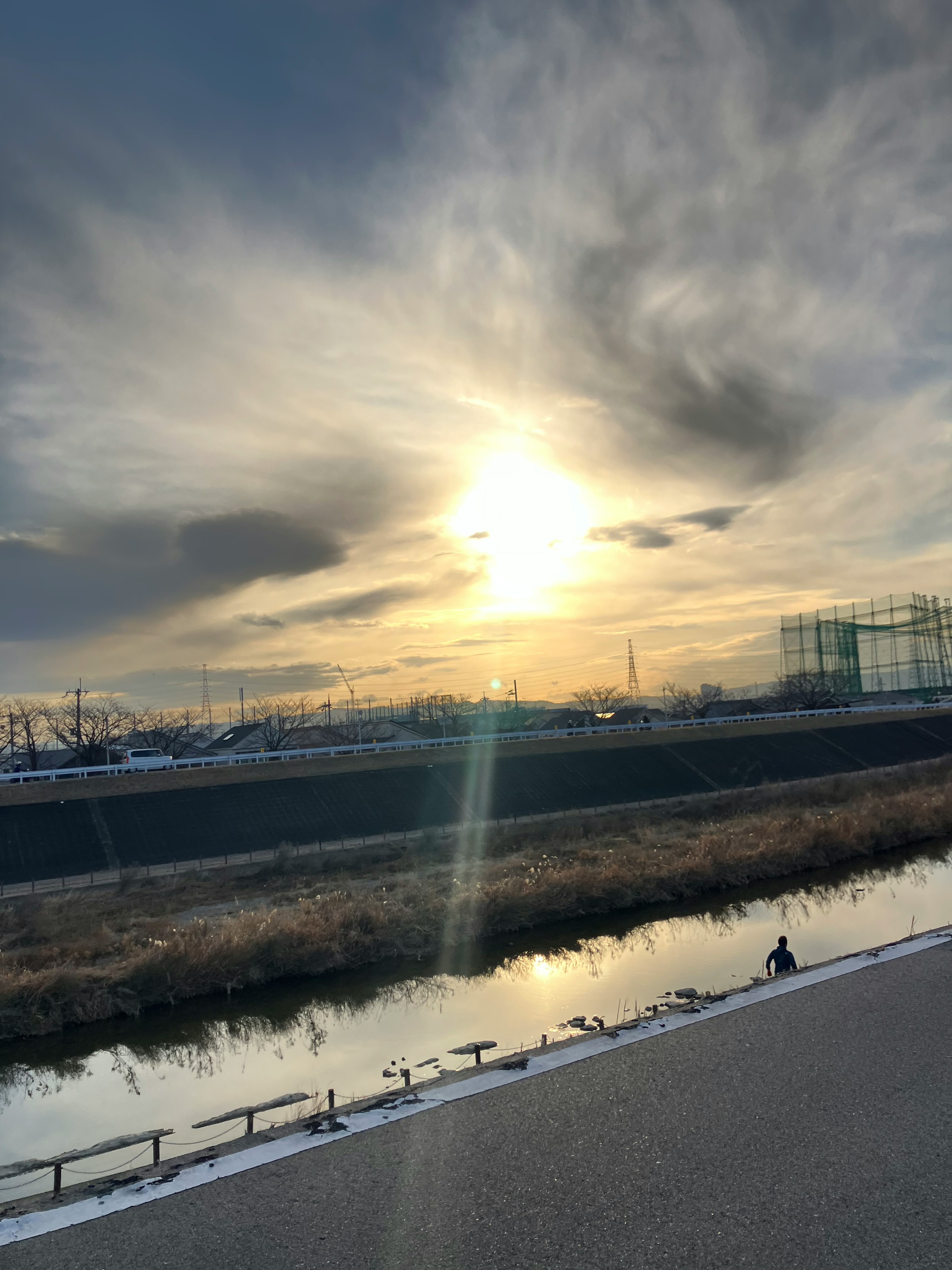 Sonnenuntergang über einem Fluss mit Wolken und entfernten Gebäuden