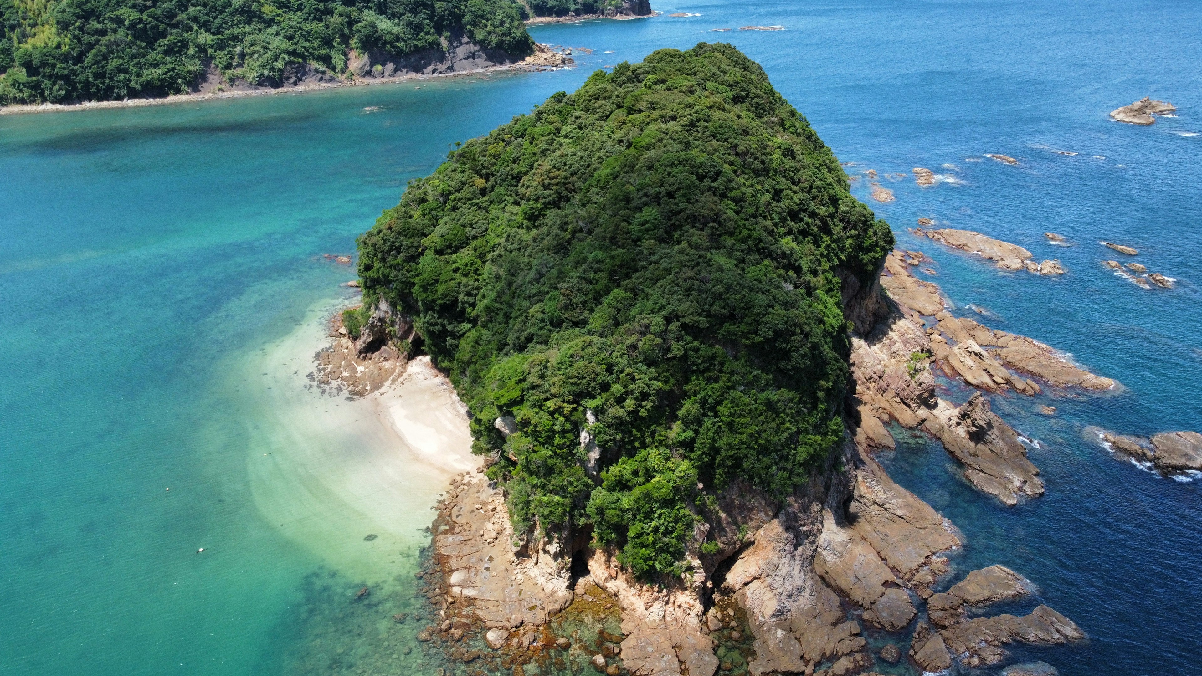 青い海に囲まれた緑豊かな小島の空撮画像