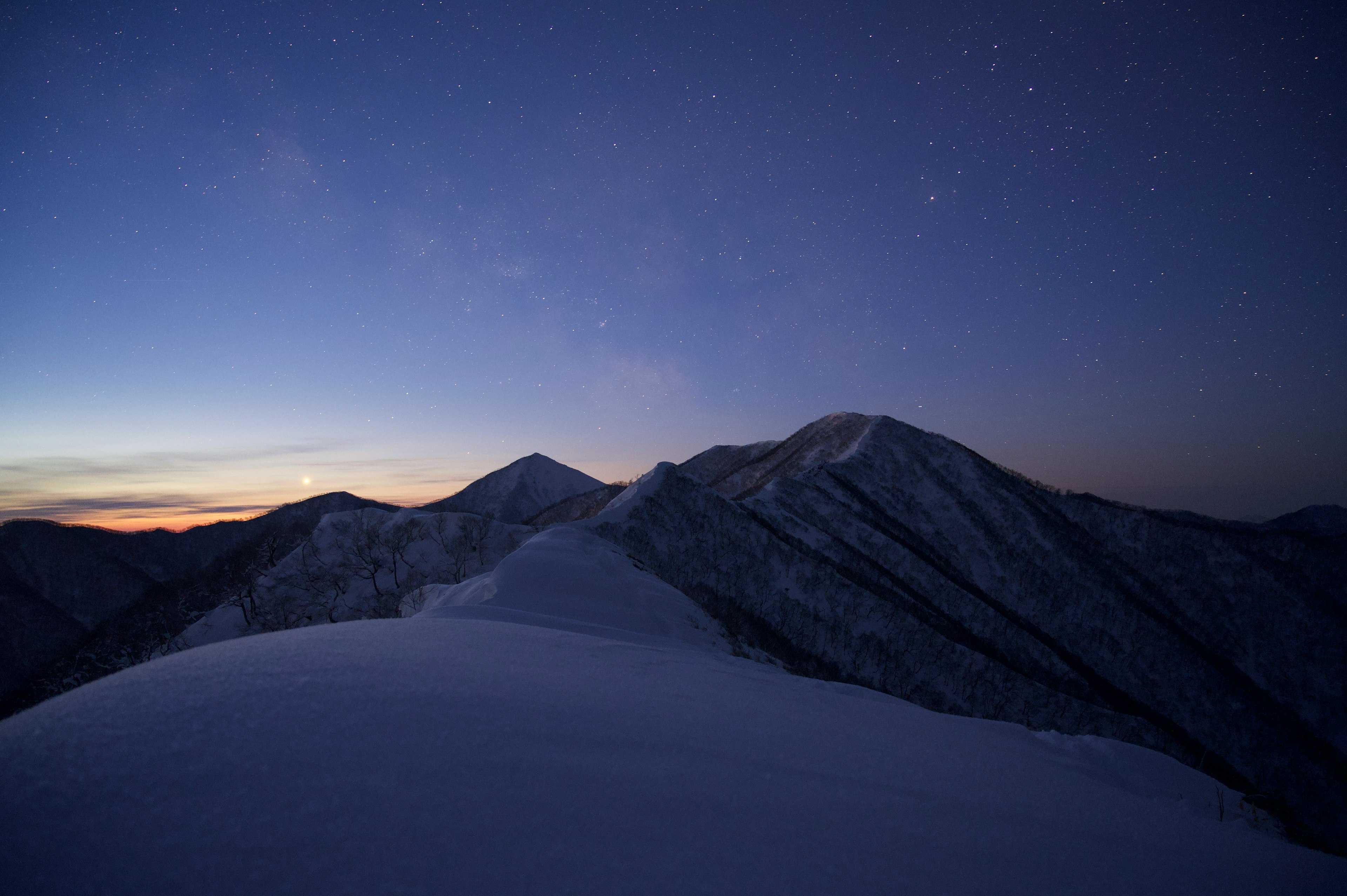 雪に覆われた山々と星空の風景が広がる夜のシーン