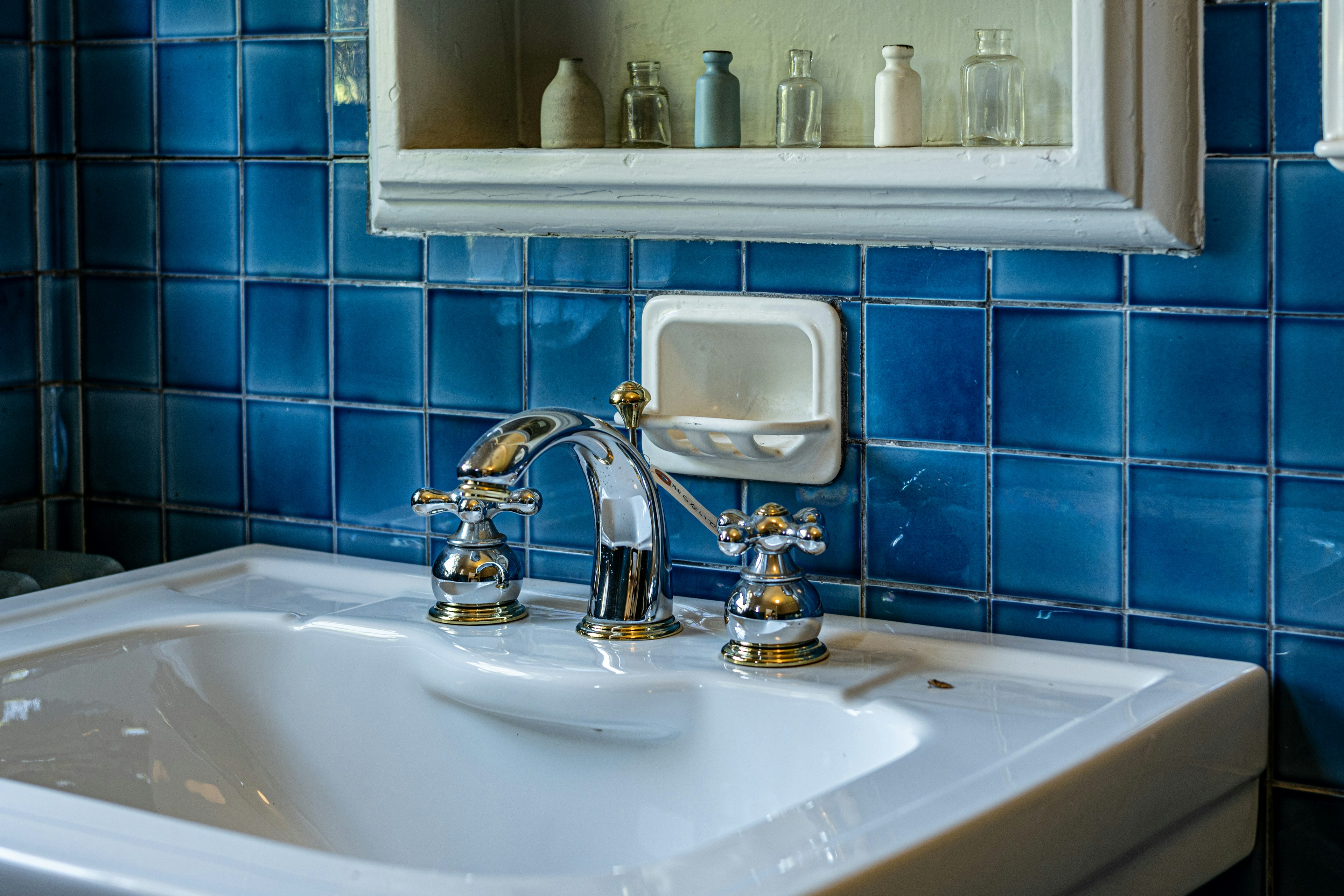 Badezimmerszene mit einem weißen Waschbecken und goldenen Wasserhähnen vor einer blauen Fliesenwand