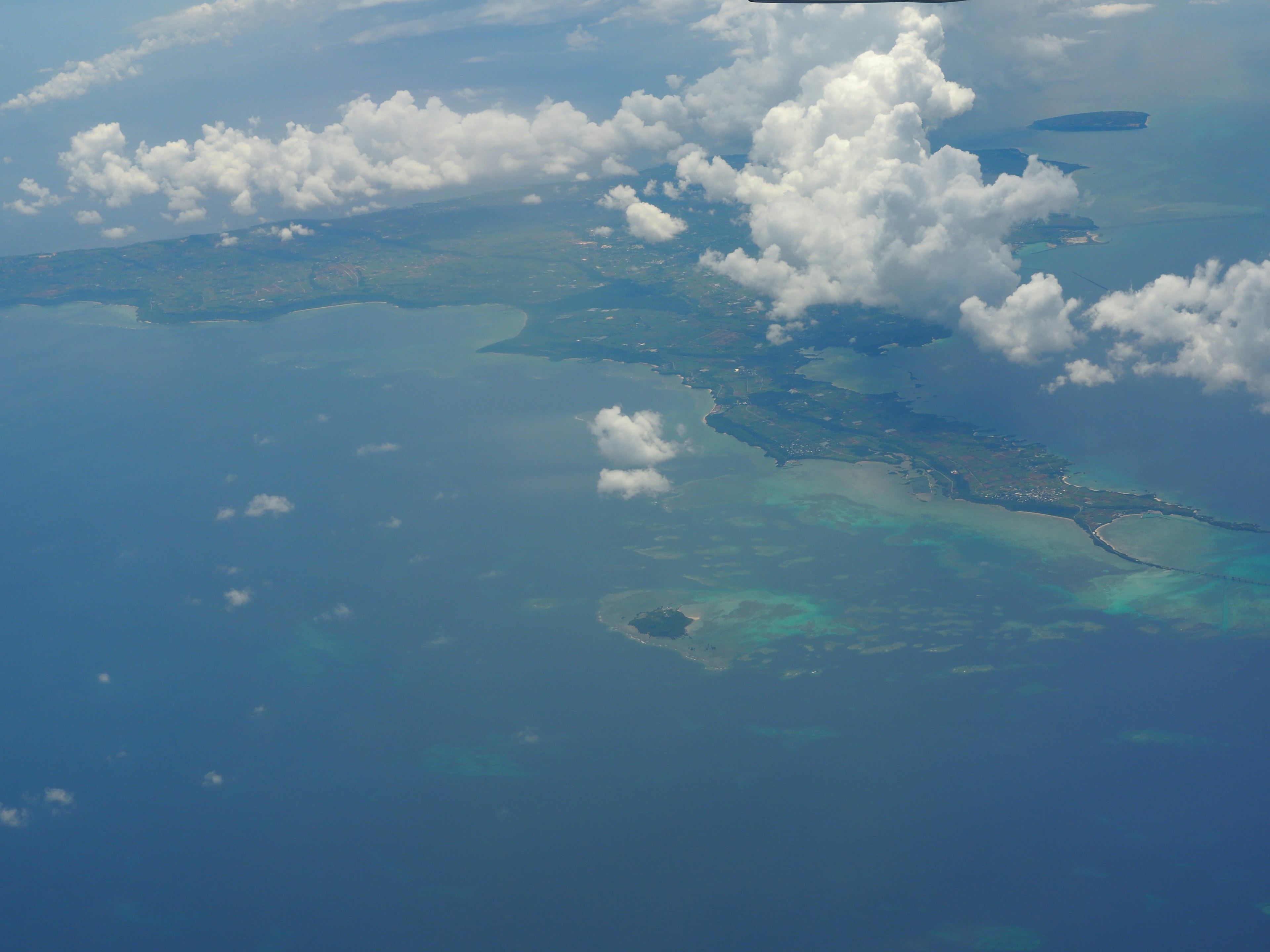 Pemandangan udara lautan biru dan awan putih dengan pulau hijau dan terumbu karang