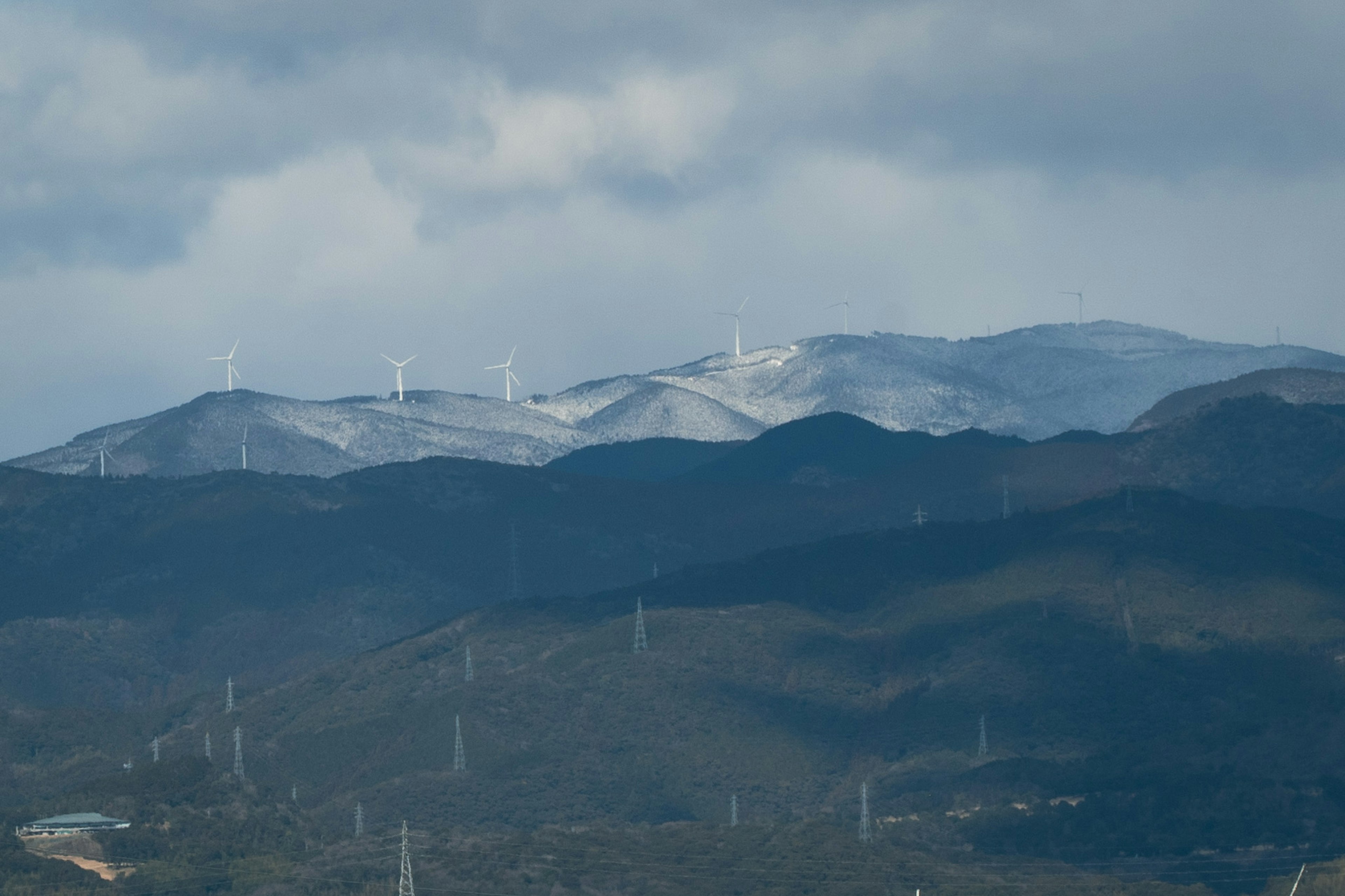 Schneebedeckte Berge mit Windkraftanlagen in der Ferne