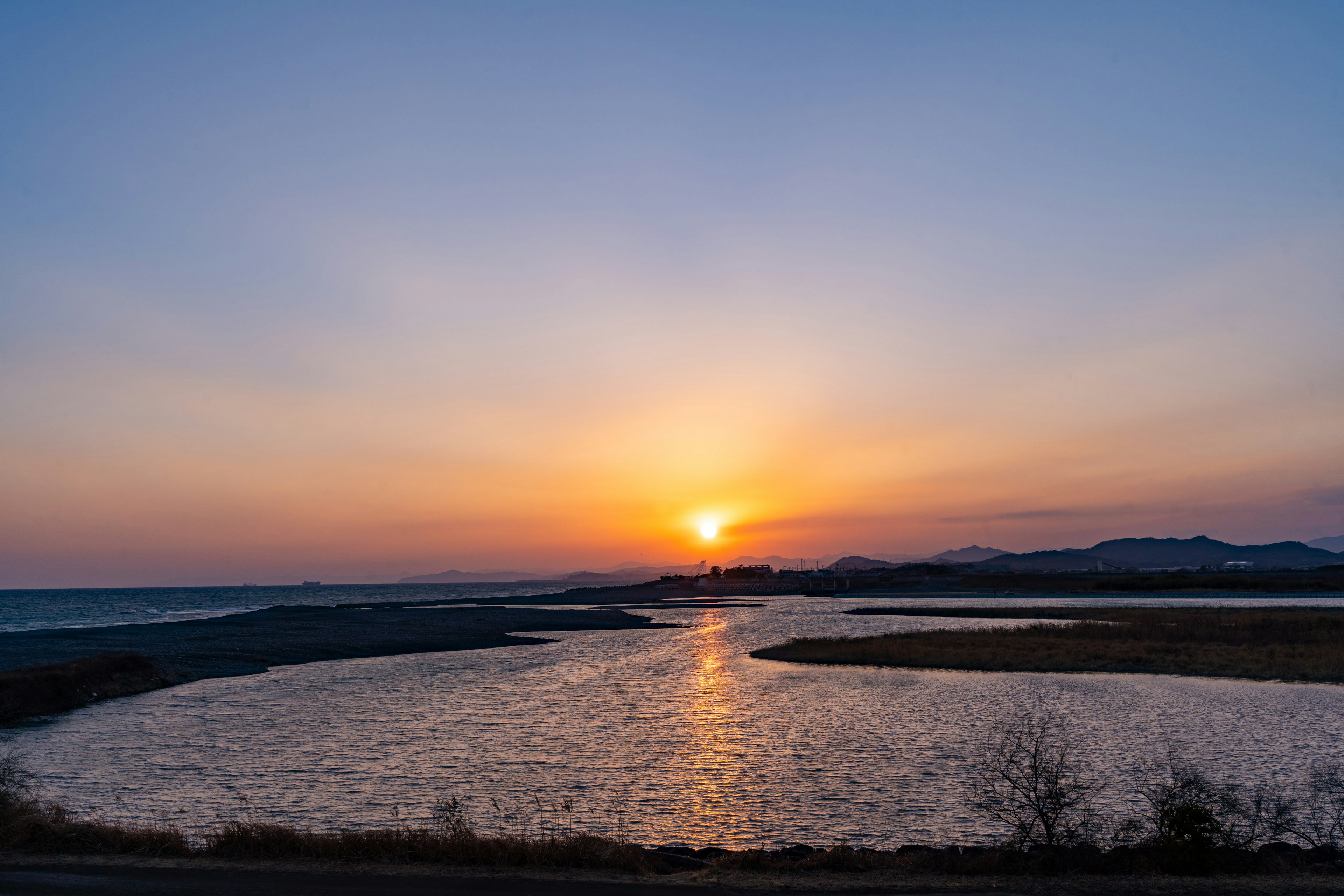 美しい夕日が海の向こうに沈む風景静かな川が流れ周囲の自然が映えています