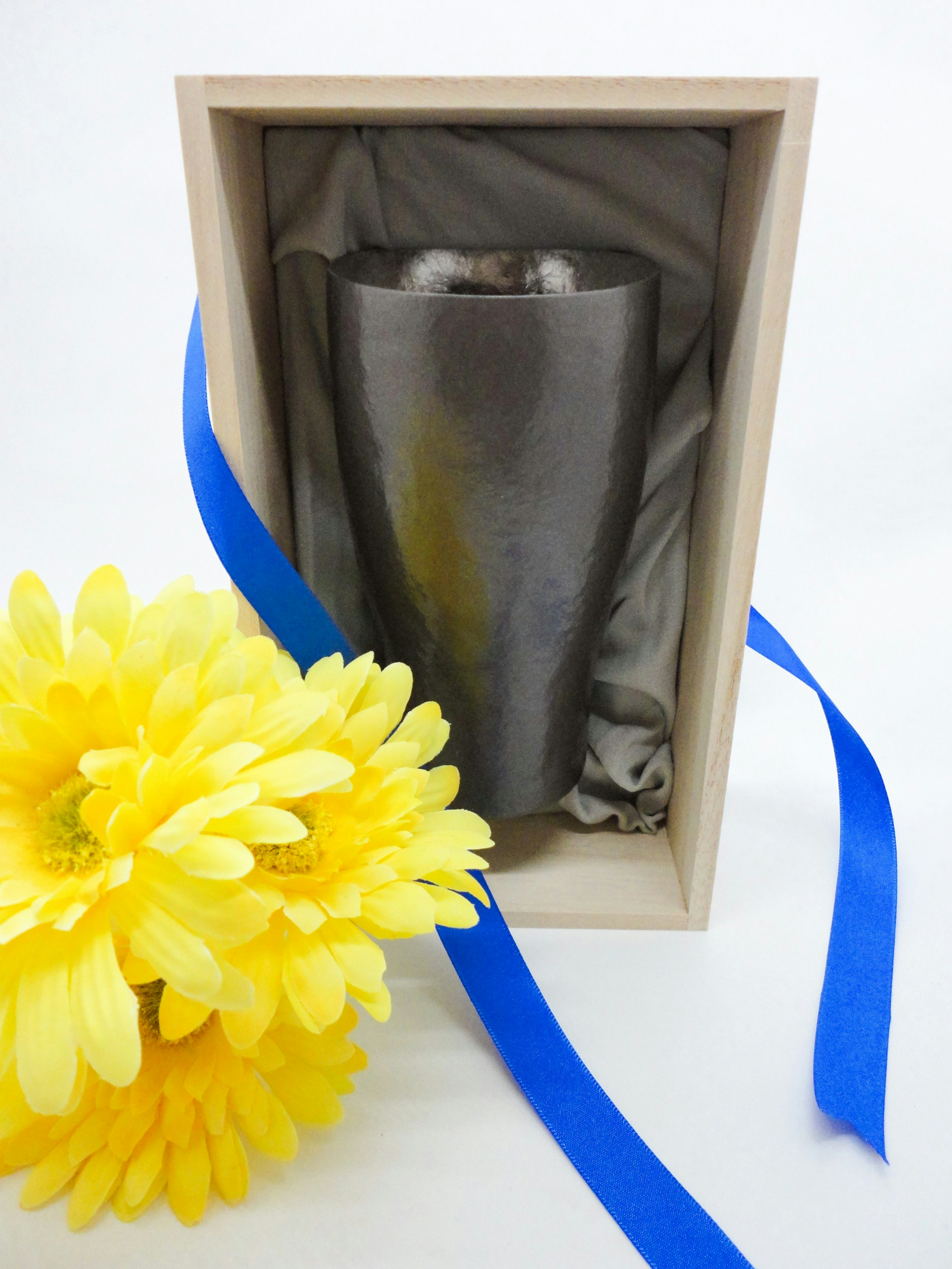 Silver object inside a wooden box with yellow flower