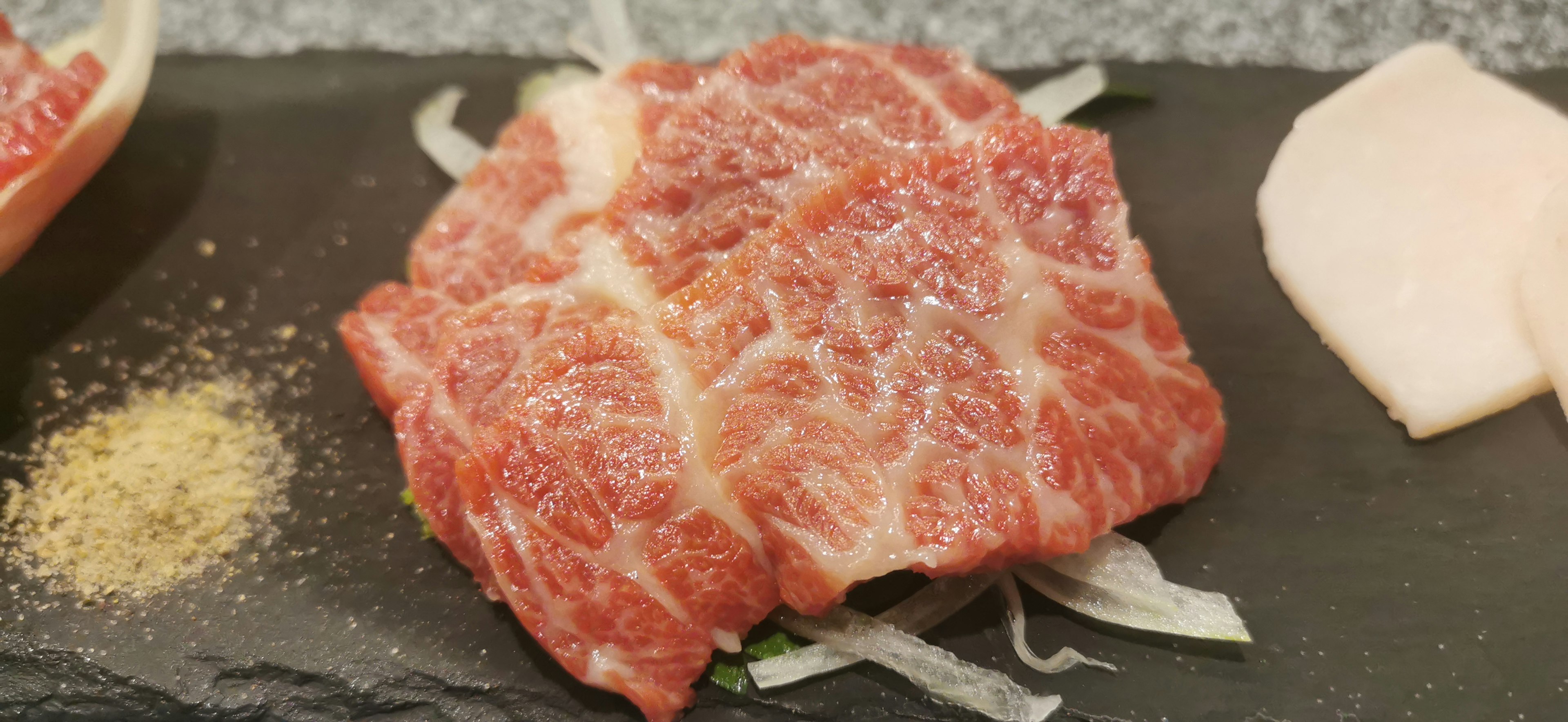 Rebanada de carne de res marmoleada en un plato negro con verduras y especias