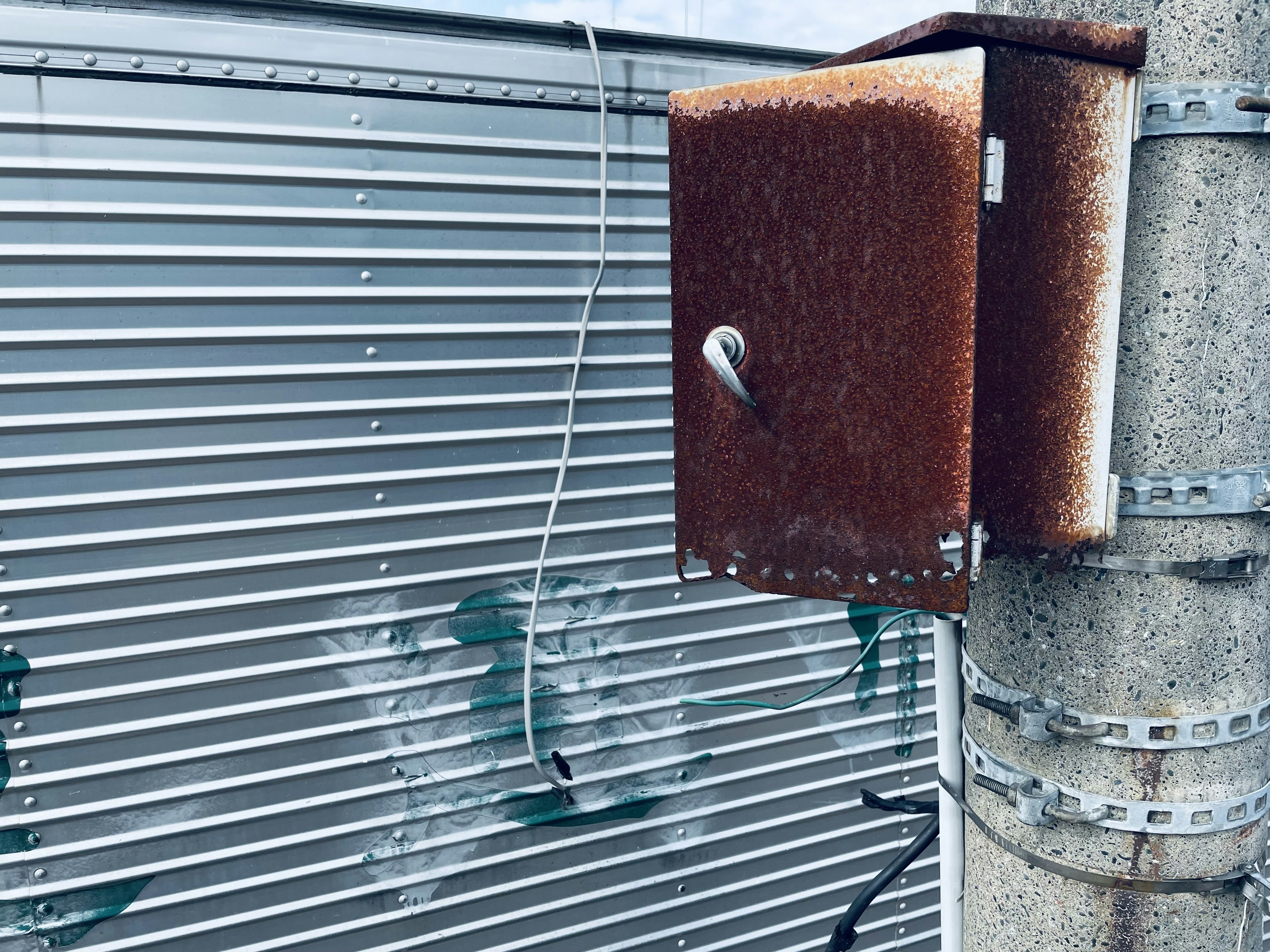 Una caja de metal oxidada unida a un poste contra un fondo a rayas plateadas