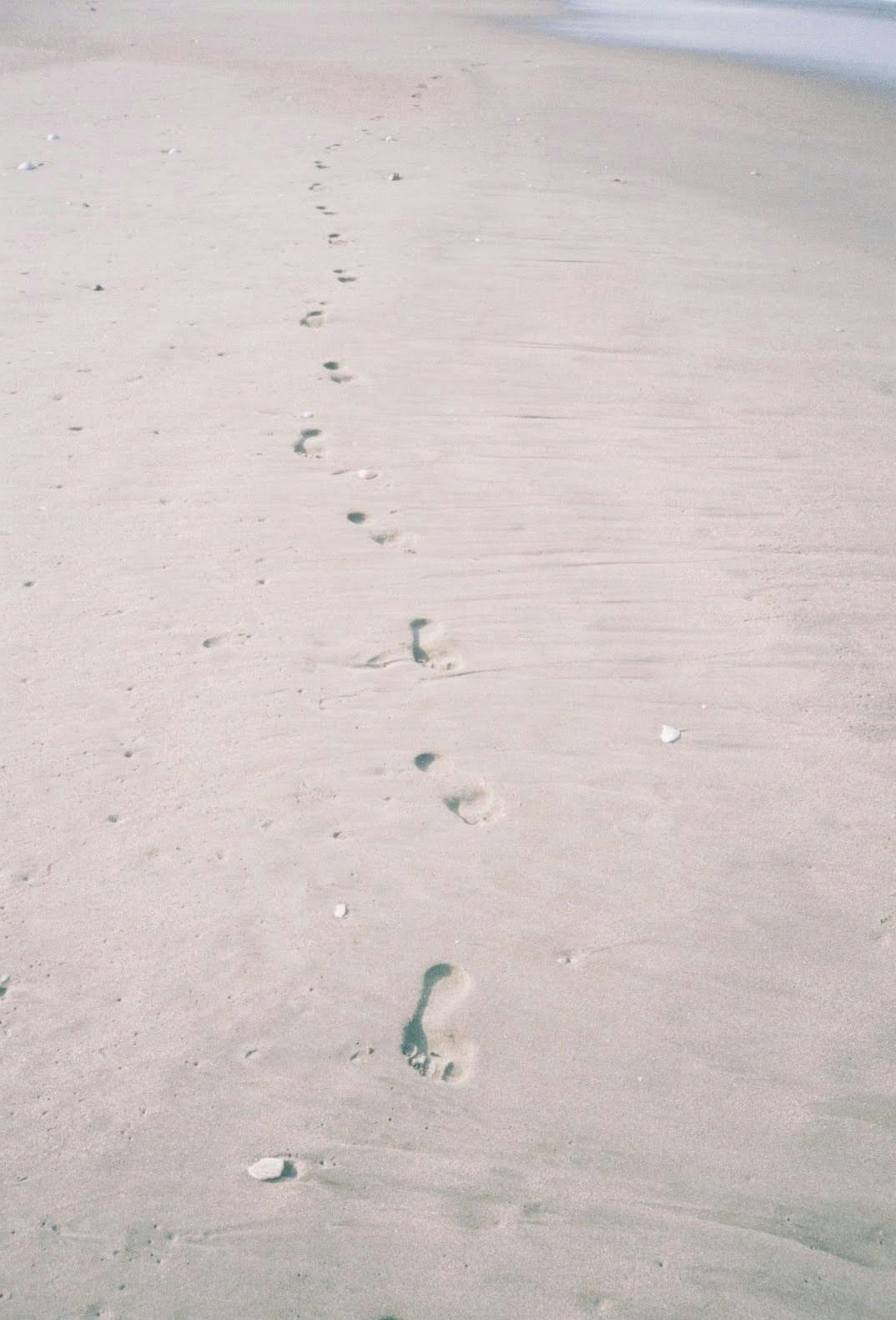 Footprints on a sandy beach leading towards the ocean