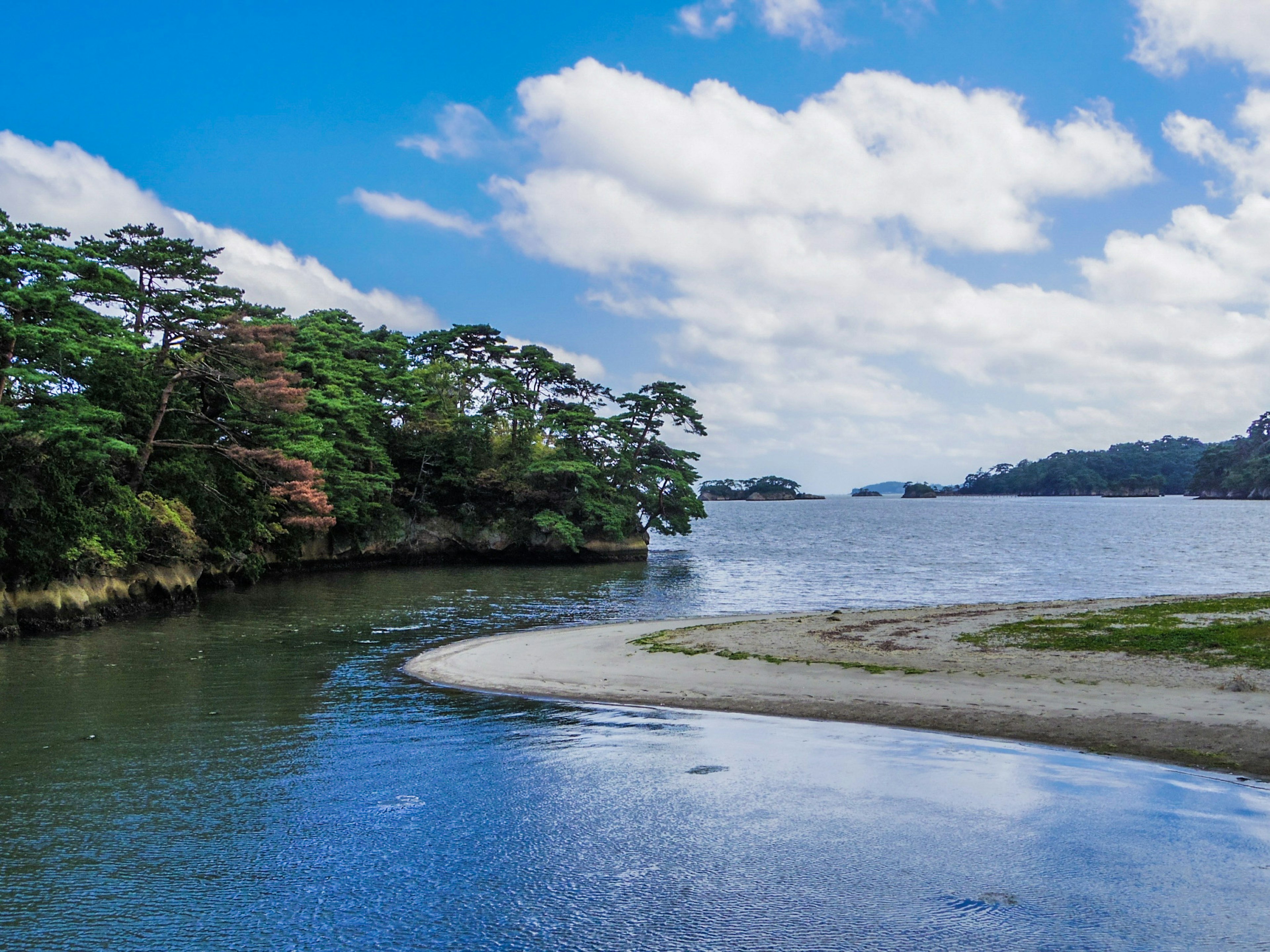 青空と雲の下の静かな水面が広がる風景 緑豊かな木々が川の両岸を彩る