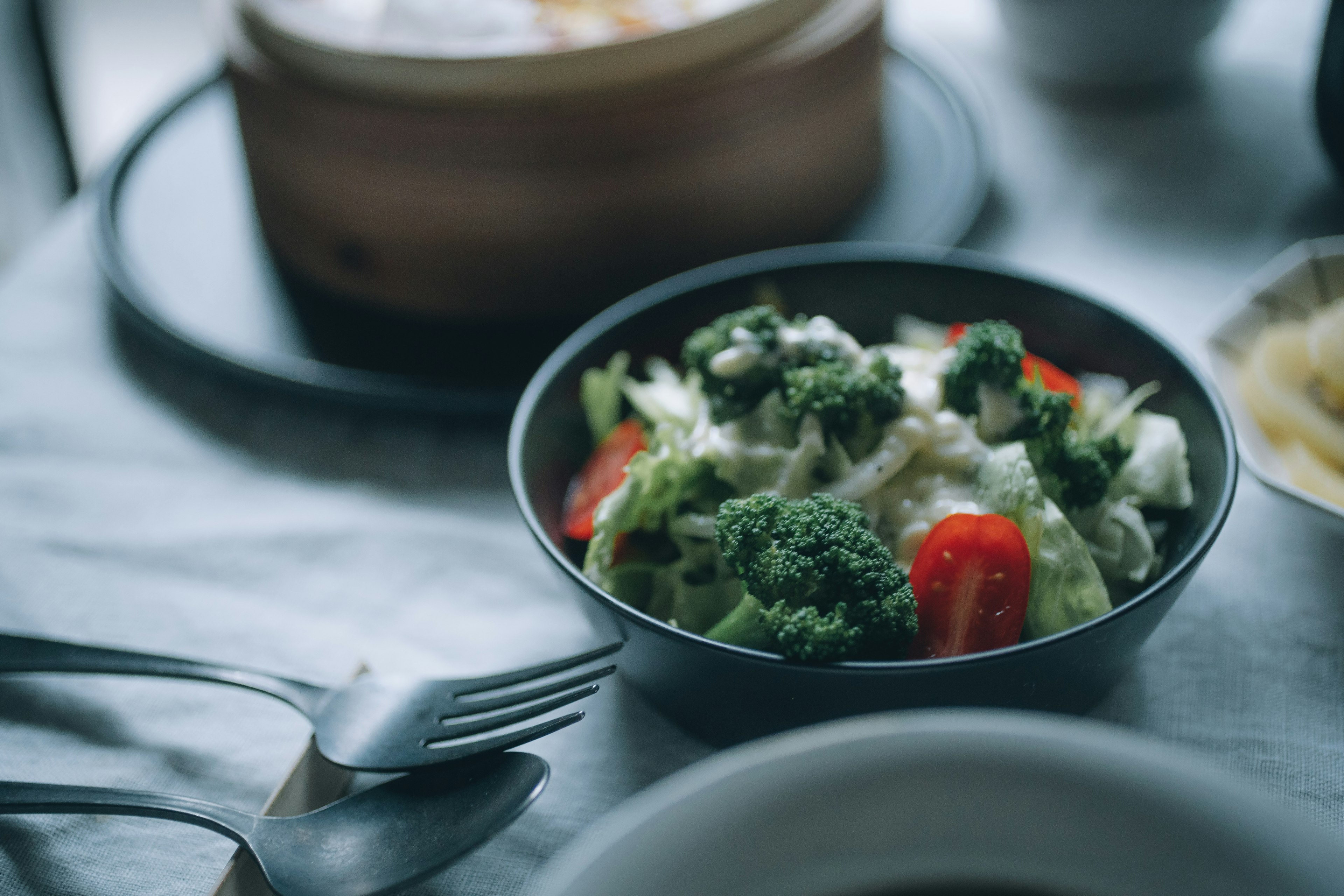 Un tazón de ensalada de verduras con brócoli y tomates en una mesa de comedor