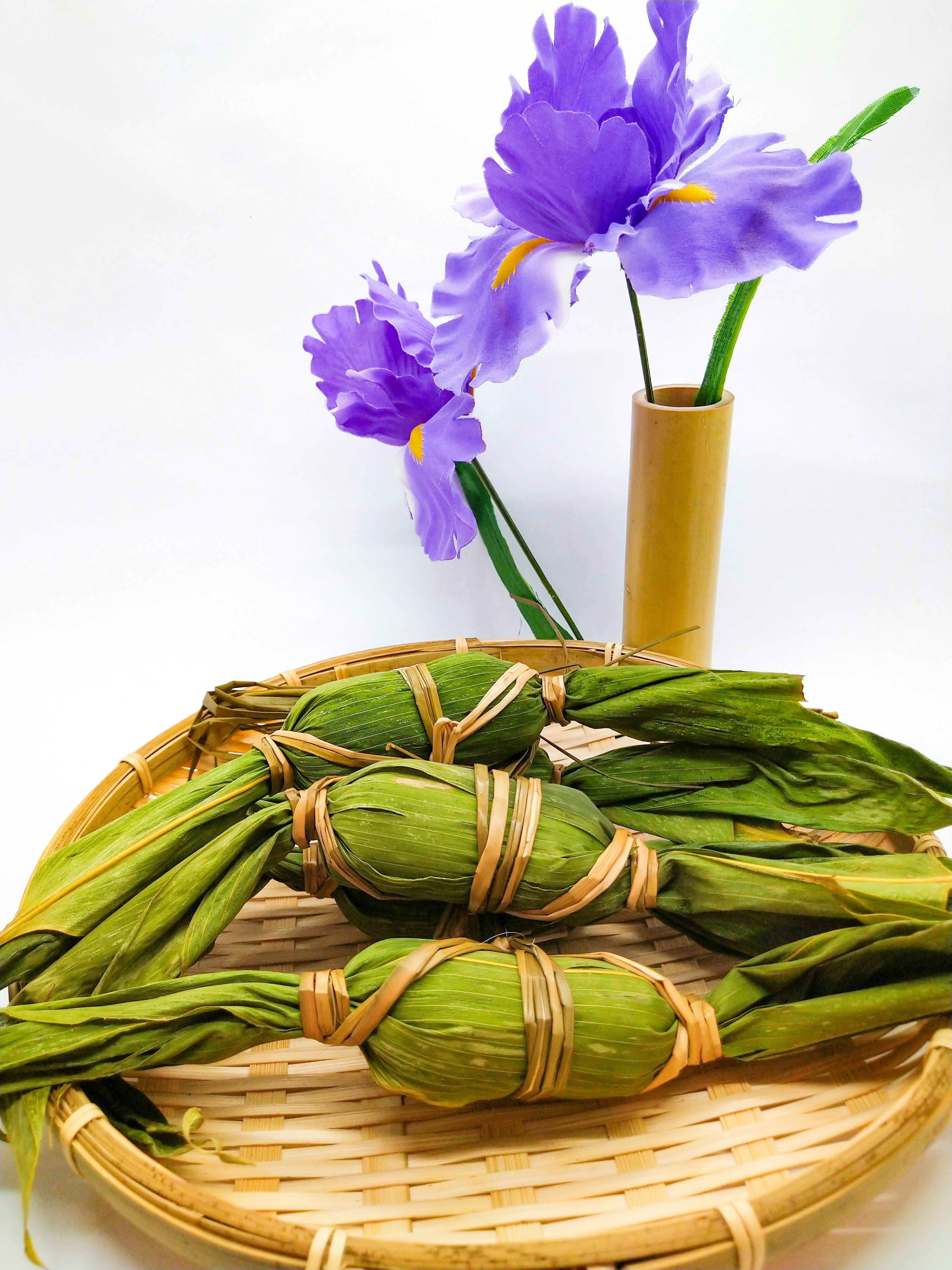 Comida tradicional envuelta en hojas verdes con flores moradas en un jarrón de bambú