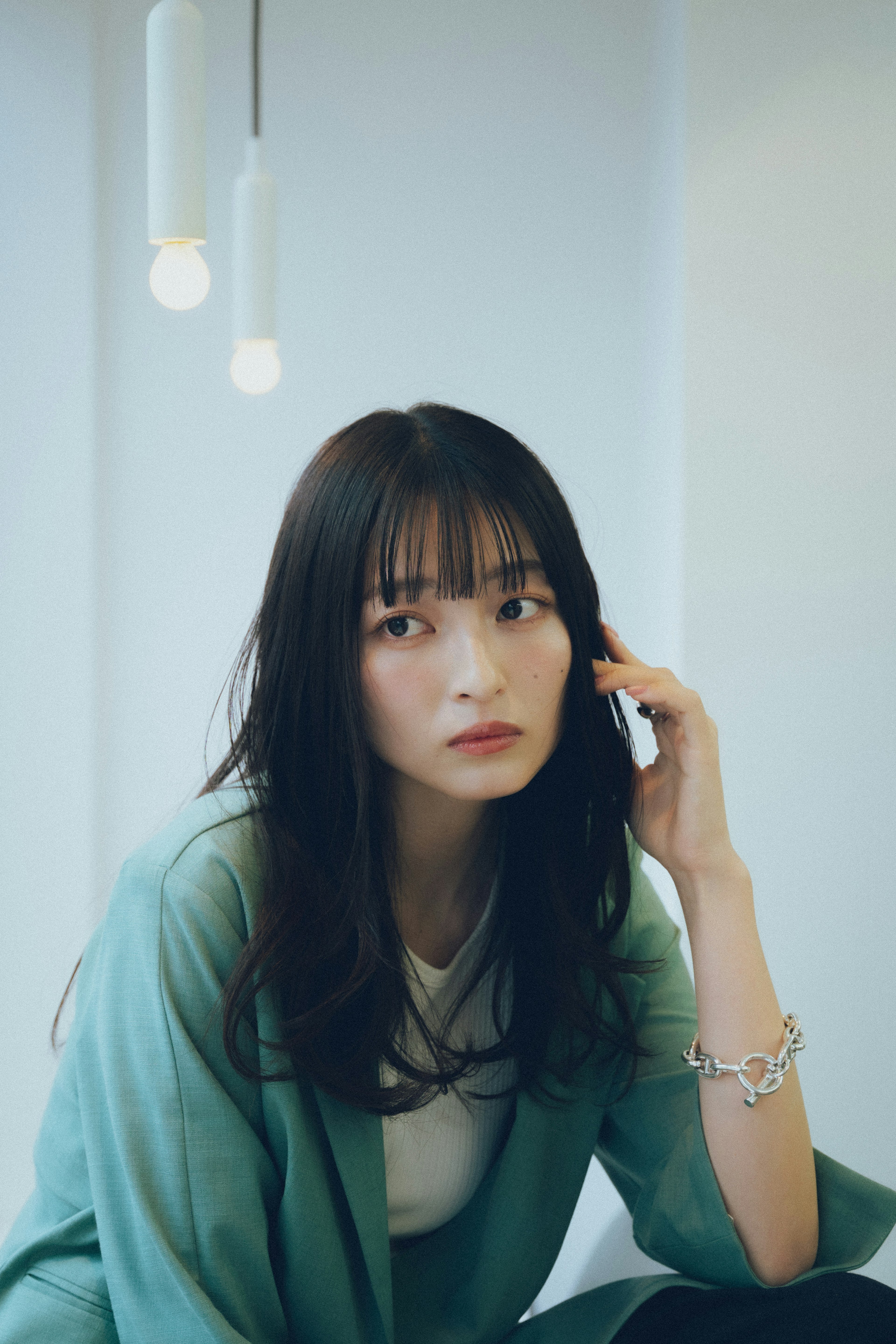 Young woman wearing a green cardigan looking thoughtfully with a bright background