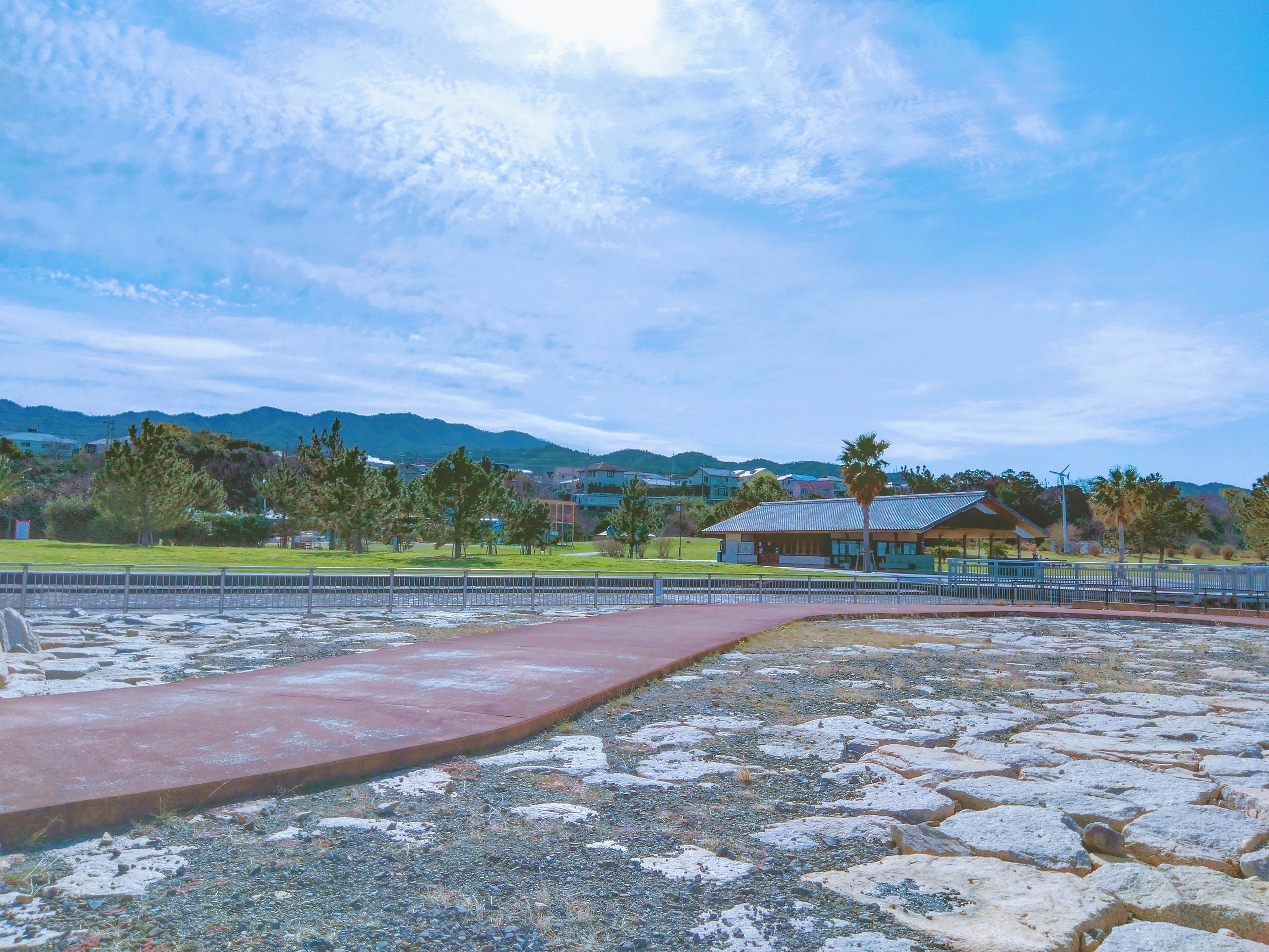 Park landscape under blue sky with mountains in the background paved path and green trees