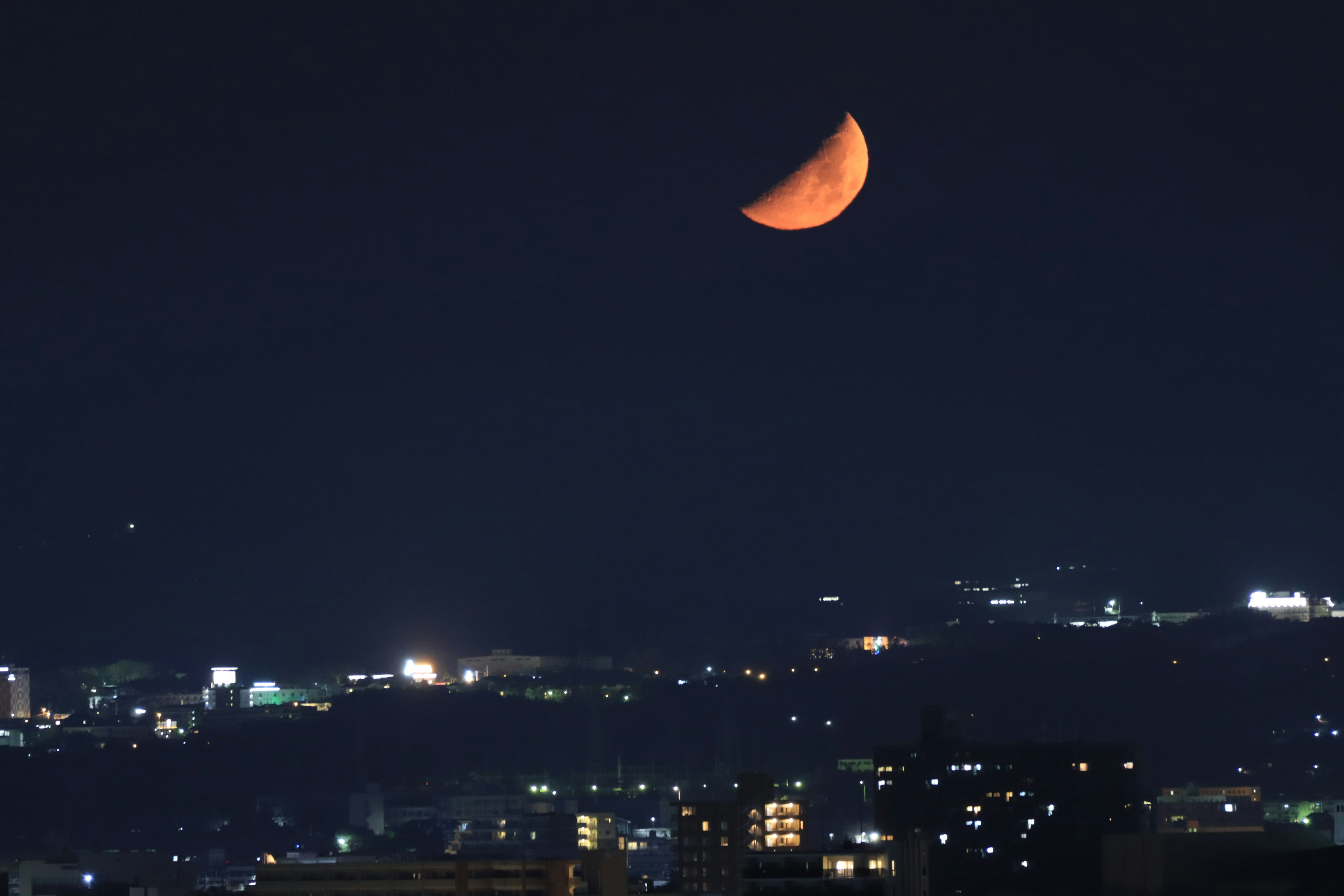 도시 불빛 위의 밤하늘에 떠 있는 주황색 초승달