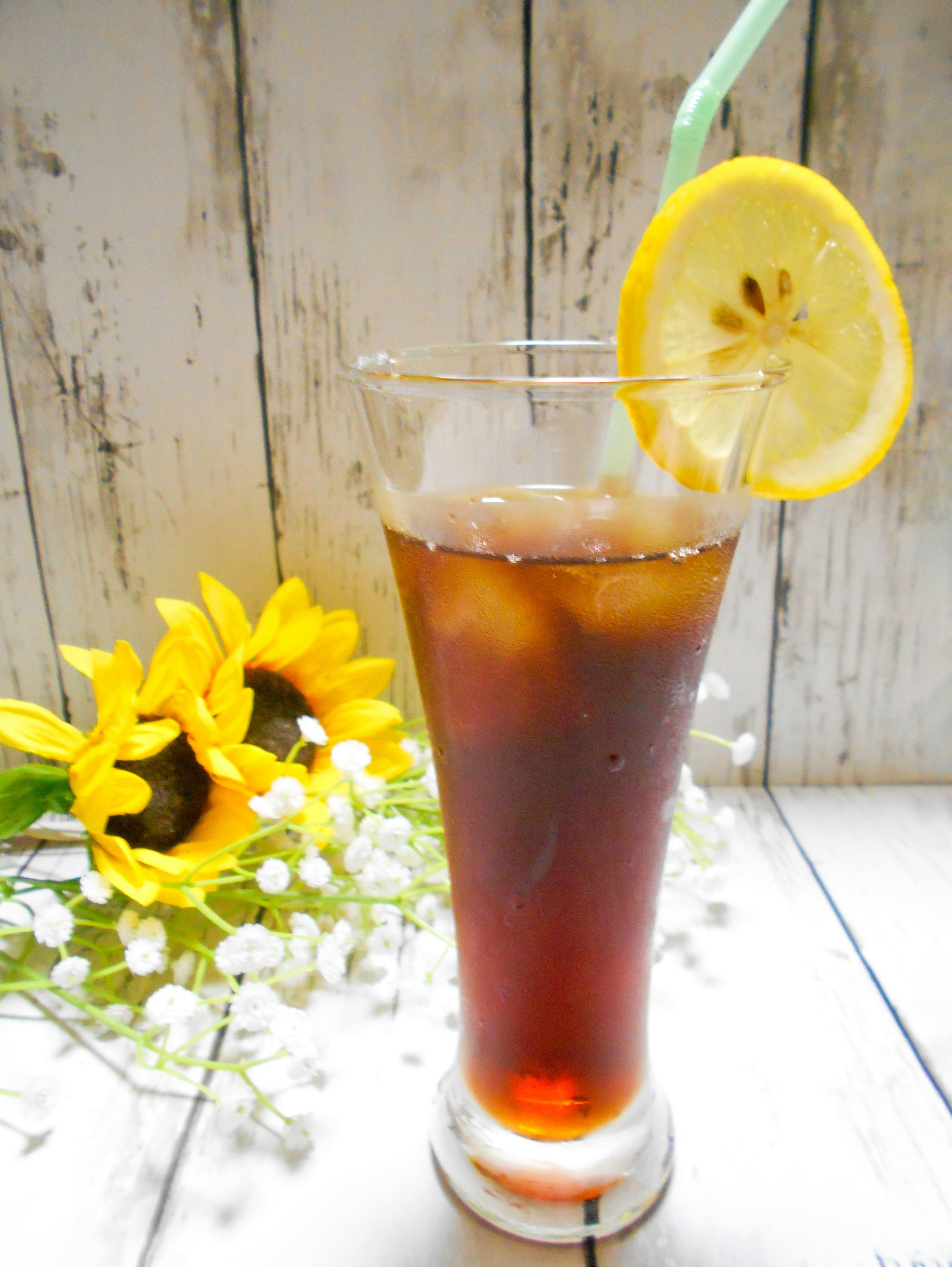 A glass of iced tea with lemon garnish and sunflowers in the background