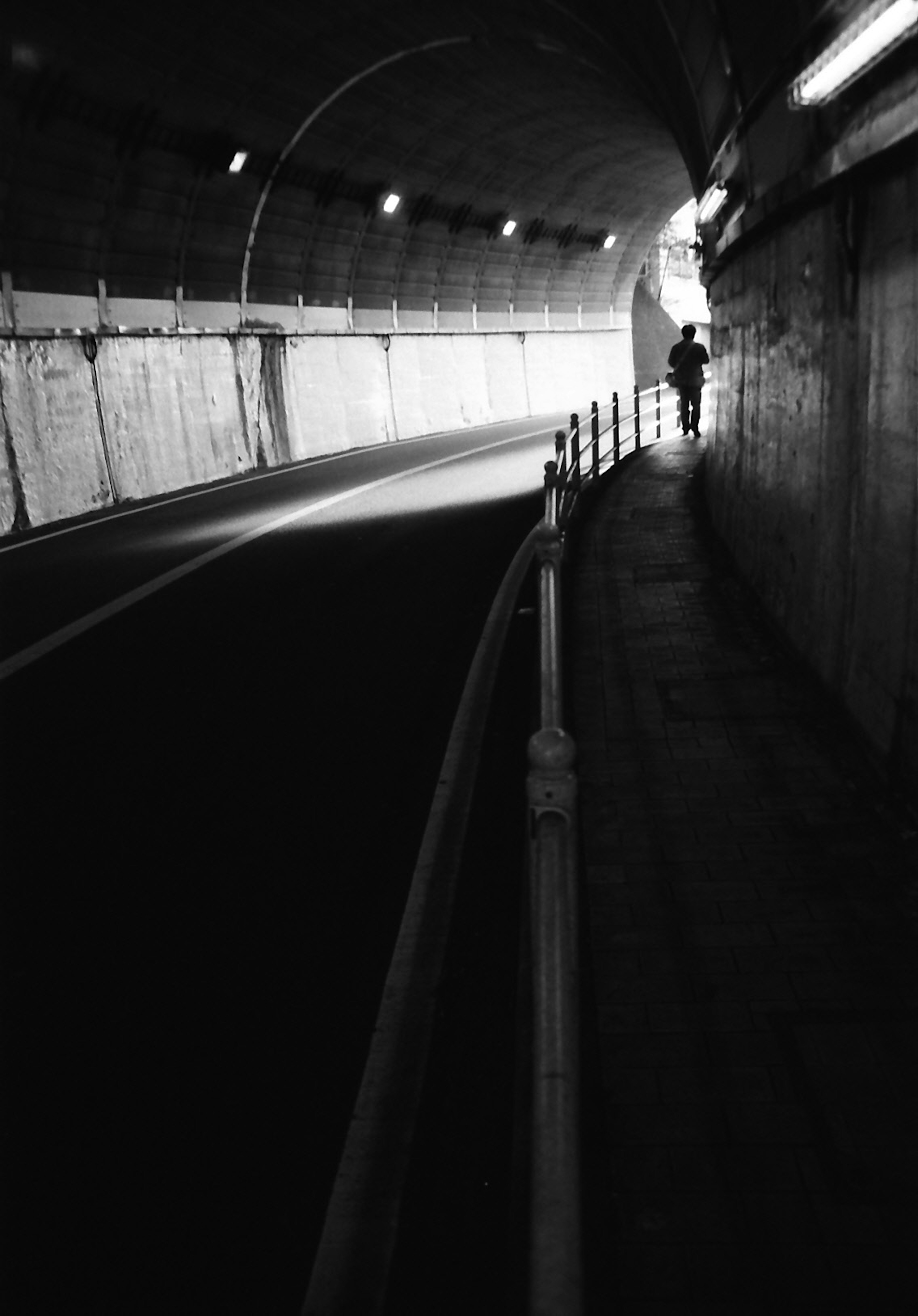 A person walking in a dark tunnel with light at the exit