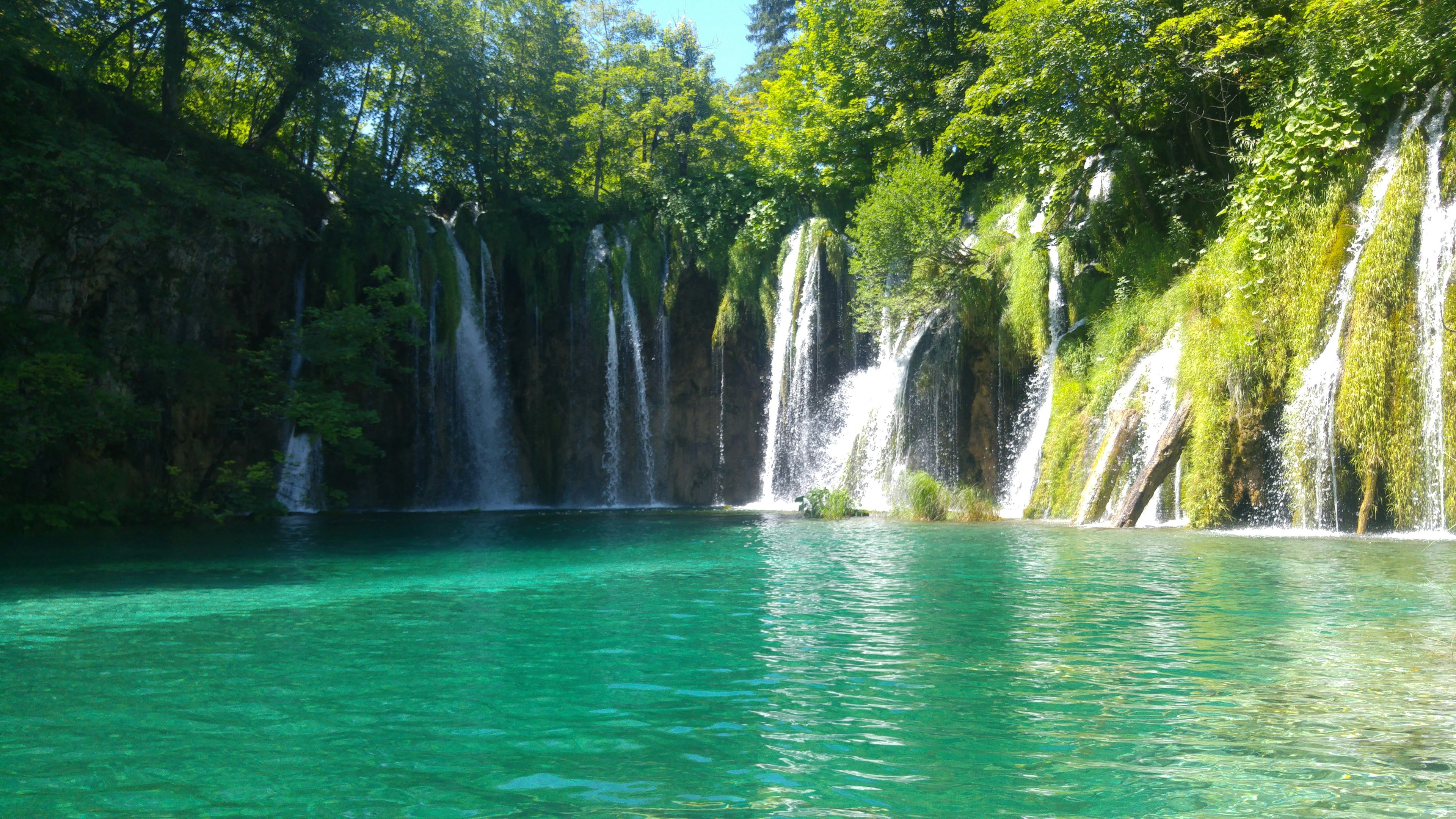 Schöner Wasserfall umgeben von blauem Wasser und grünen Bäumen