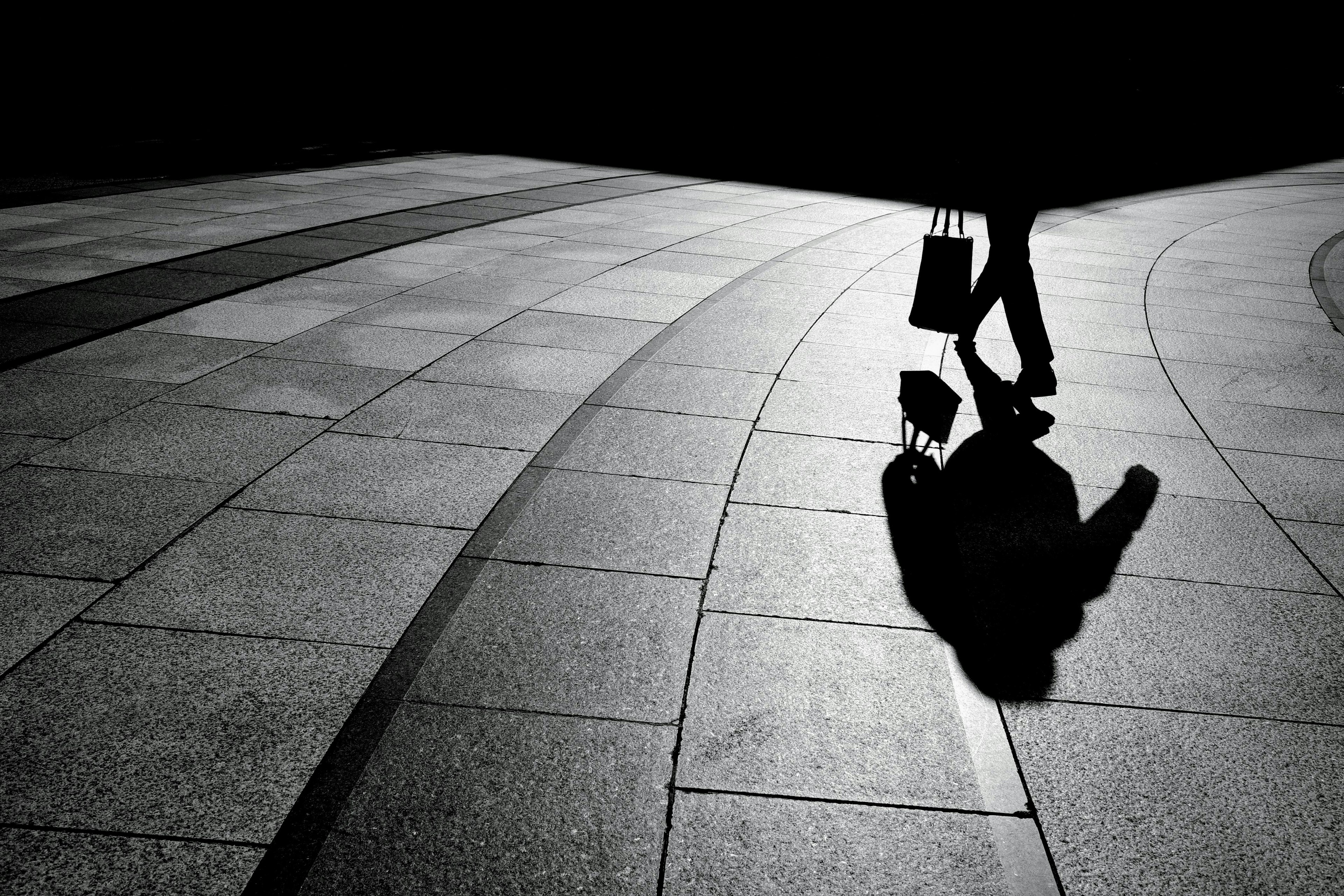 Una persona caminando en sombras con su reflejo en un pavimento curvado