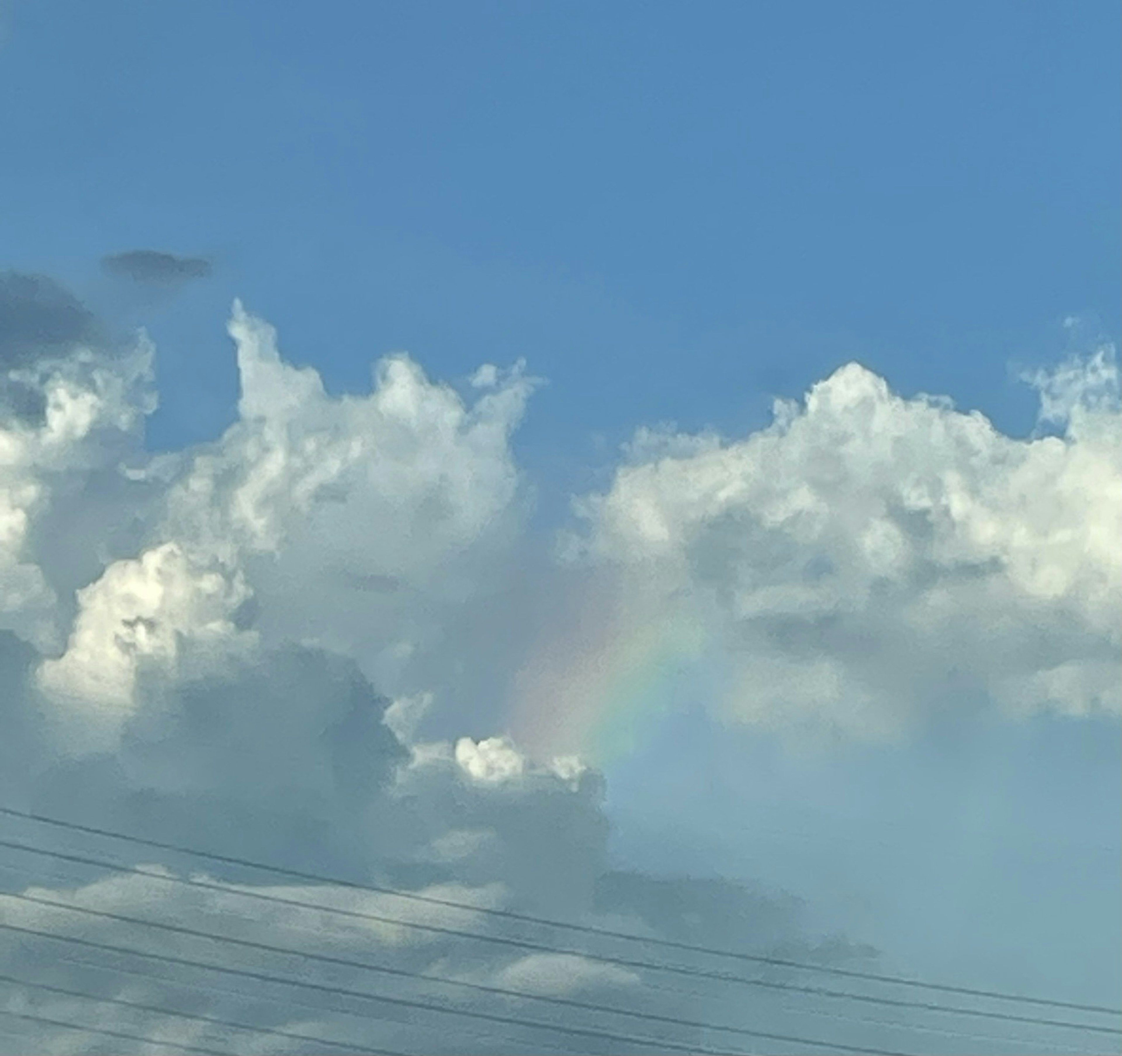 Part of a rainbow appearing among fluffy clouds in a blue sky