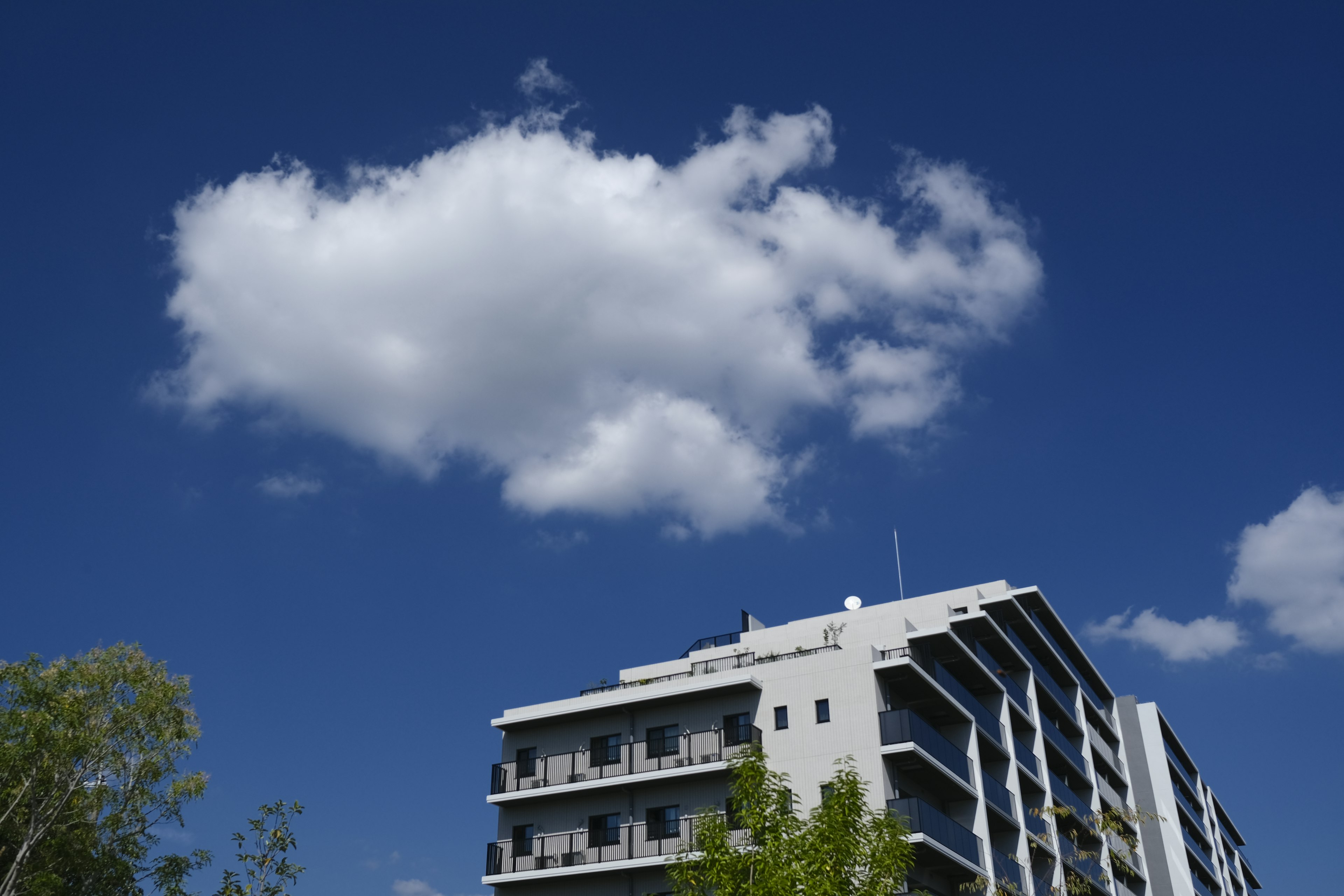 Bangunan modern di bawah langit biru cerah dengan awan putih berbulu