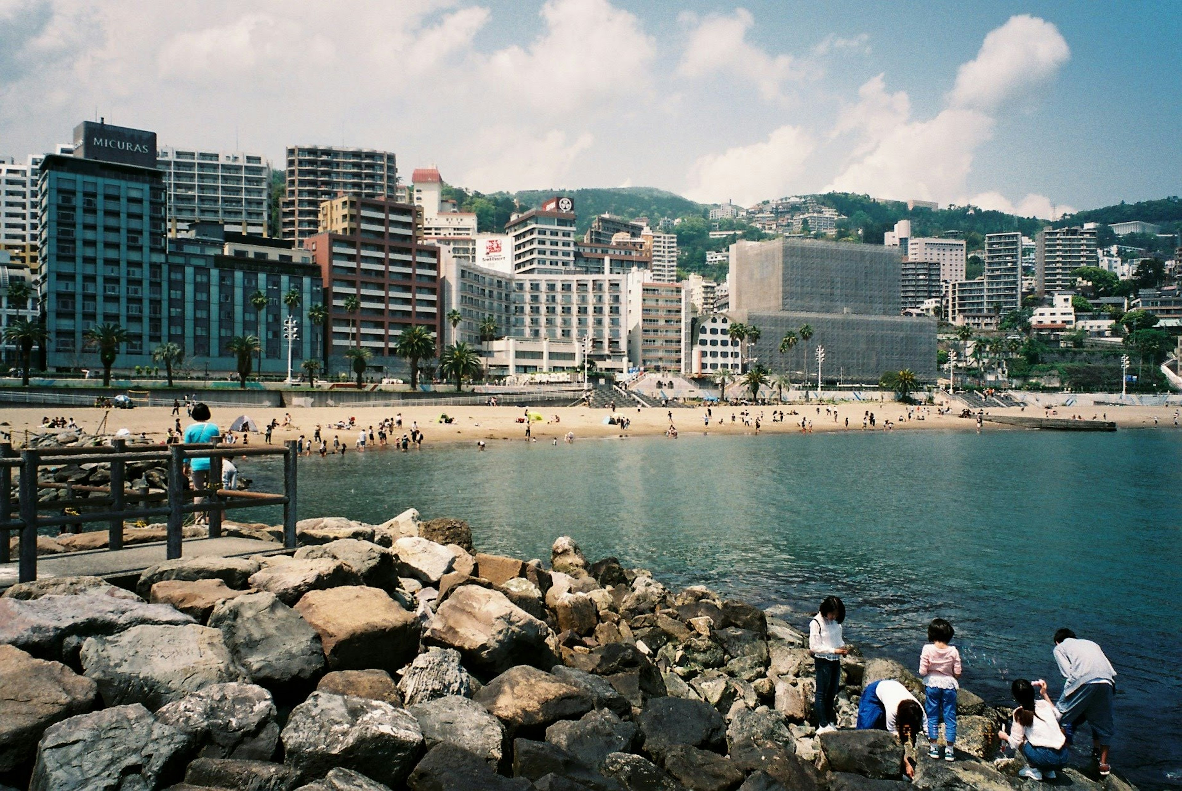 Escena costera con paisaje urbano y personas sentadas en rocas