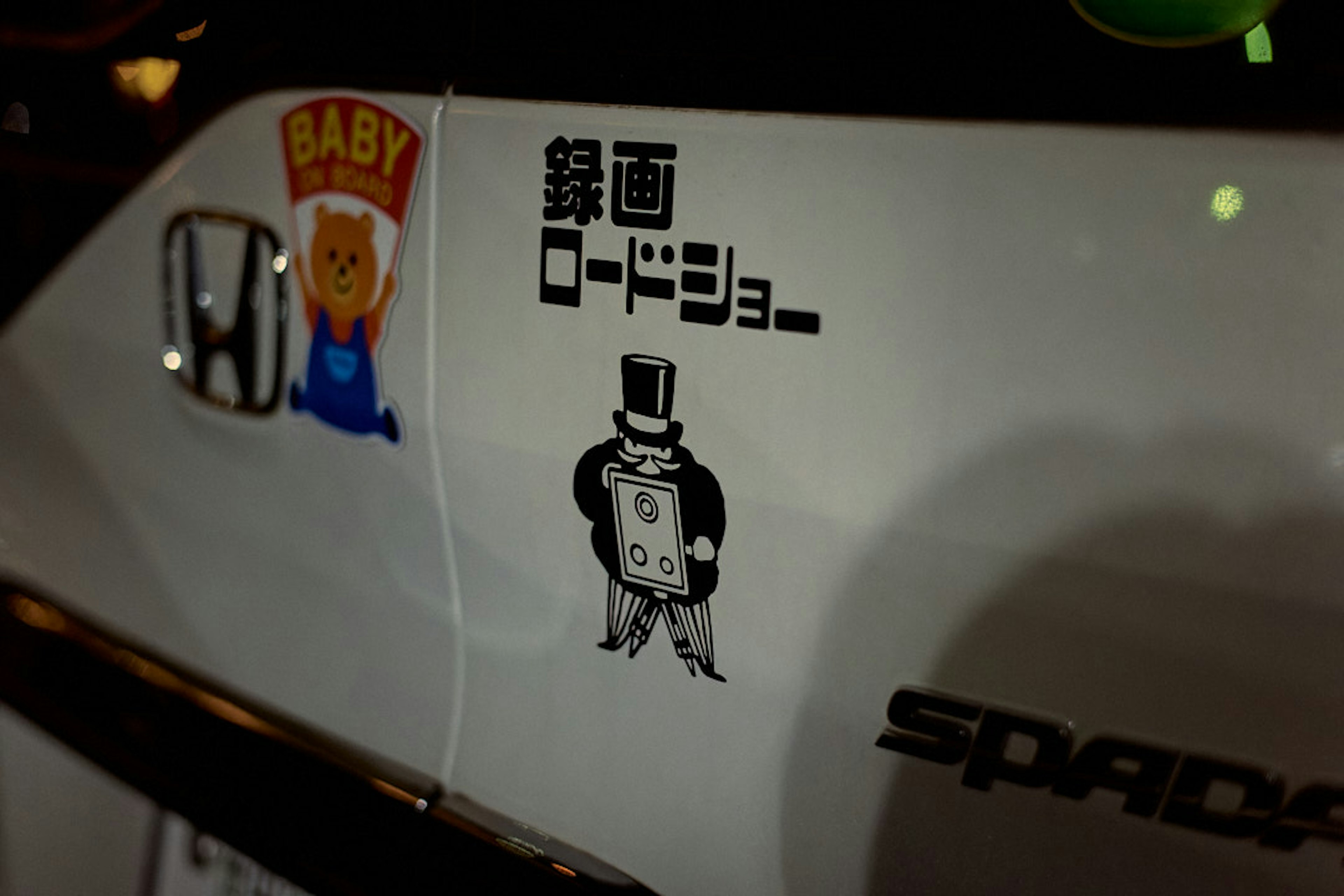 Sticker en el costado de un coche blanco que presenta un personaje de bebé y un hombre con sombrero de copa