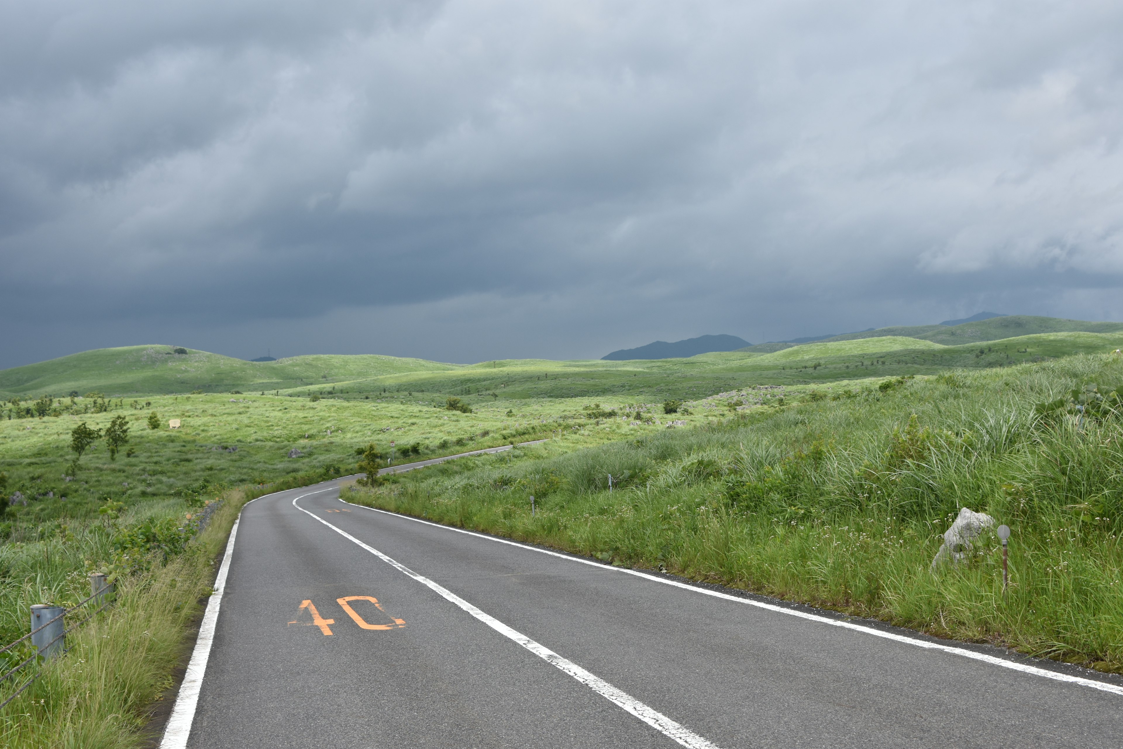 Winding road through green hills under dark clouds