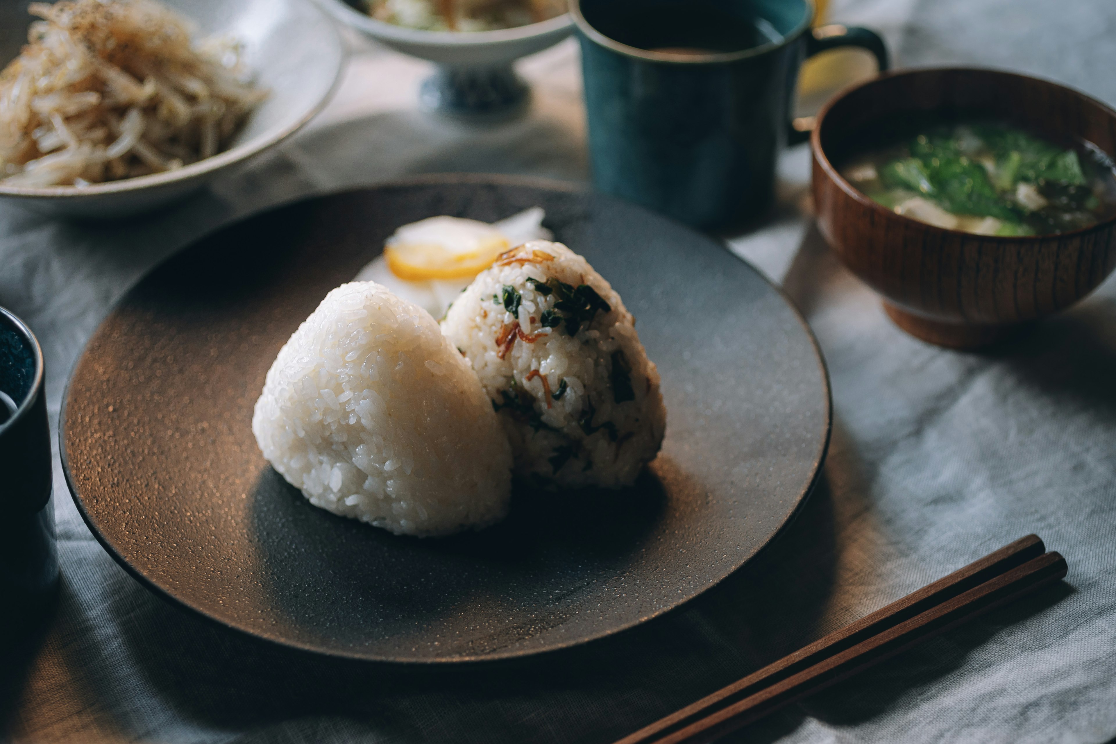 Japanese meal featuring rice balls and grilled fish on a dark plate