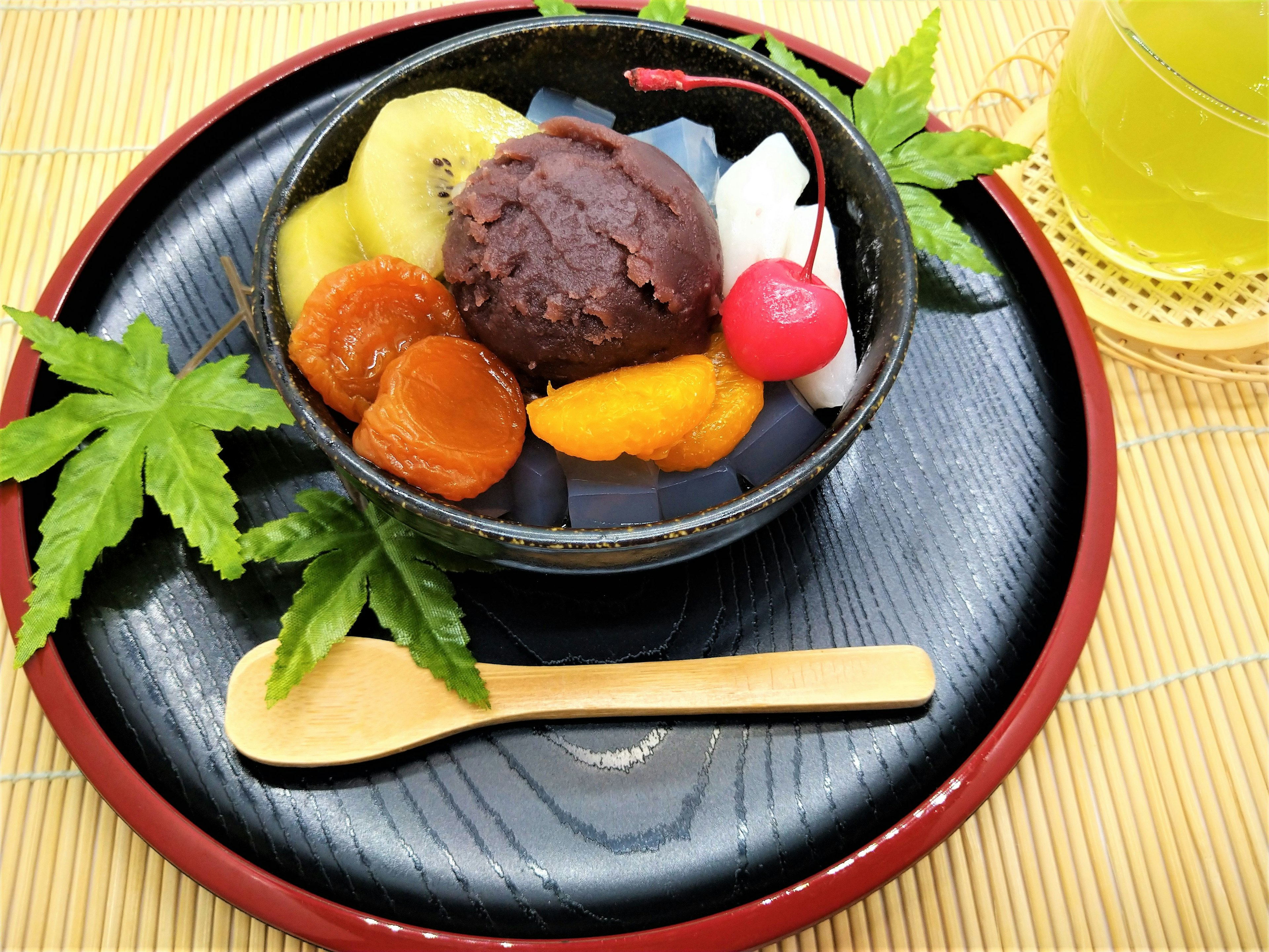 Assorted Japanese sweets and ice cream in a black bowl Green tea and bamboo mat in the background