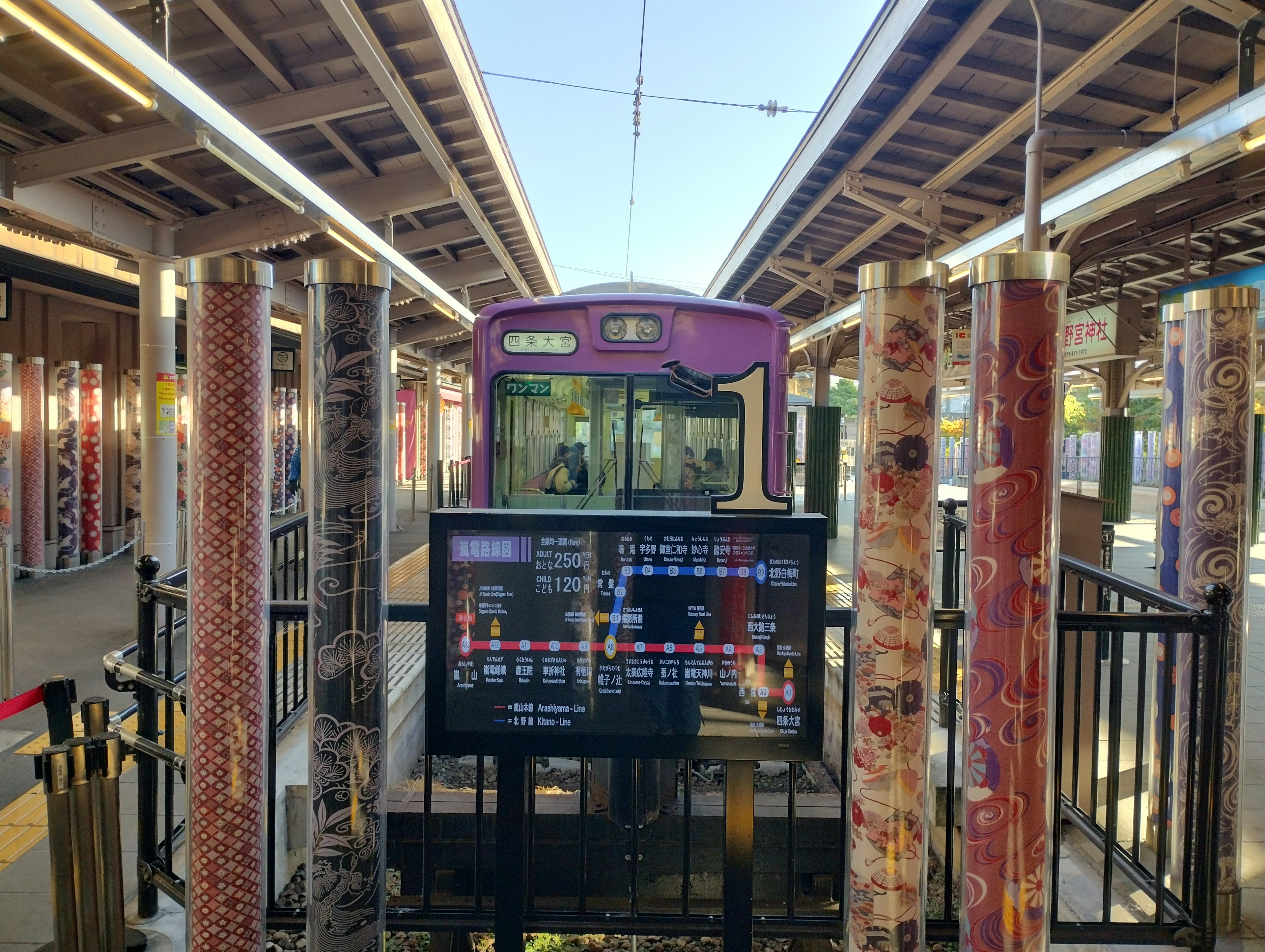 Bunte Säulen umgeben einen Bahnhof mit einem lila Zug am Bahnsteig