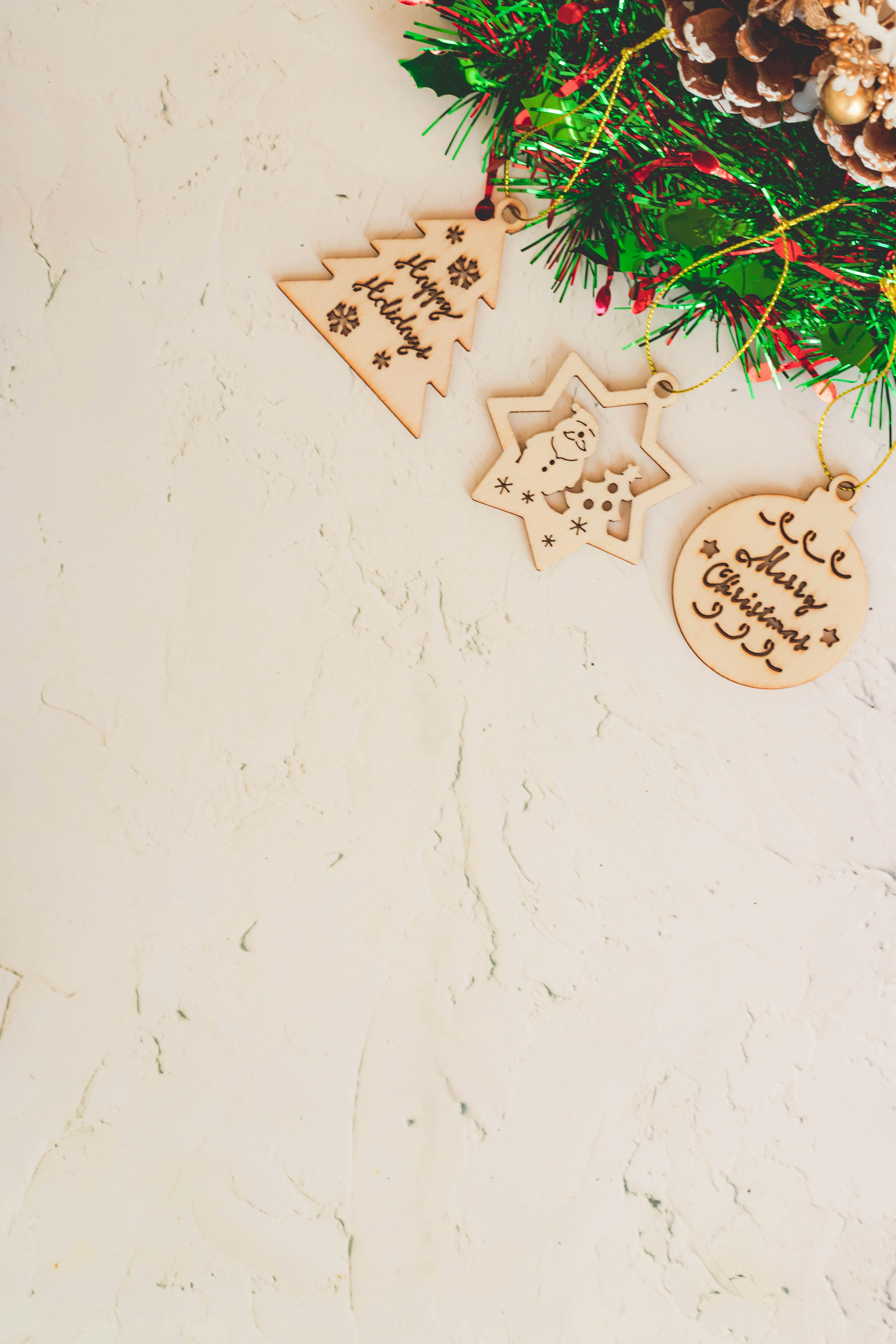 Adornos navideños de madera colgando de una corona verde con piñas