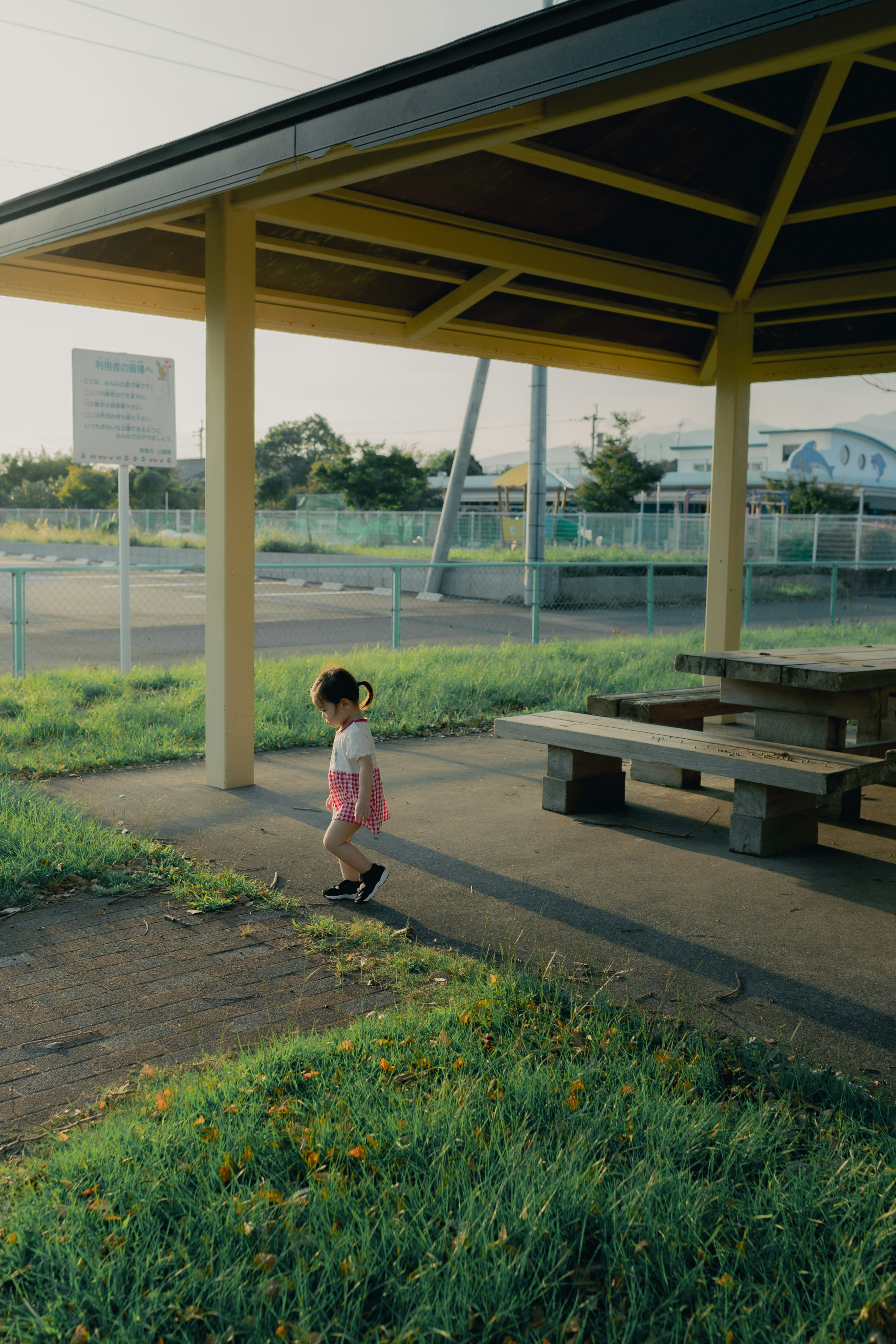 A small girl walking near a pavilion with a roof