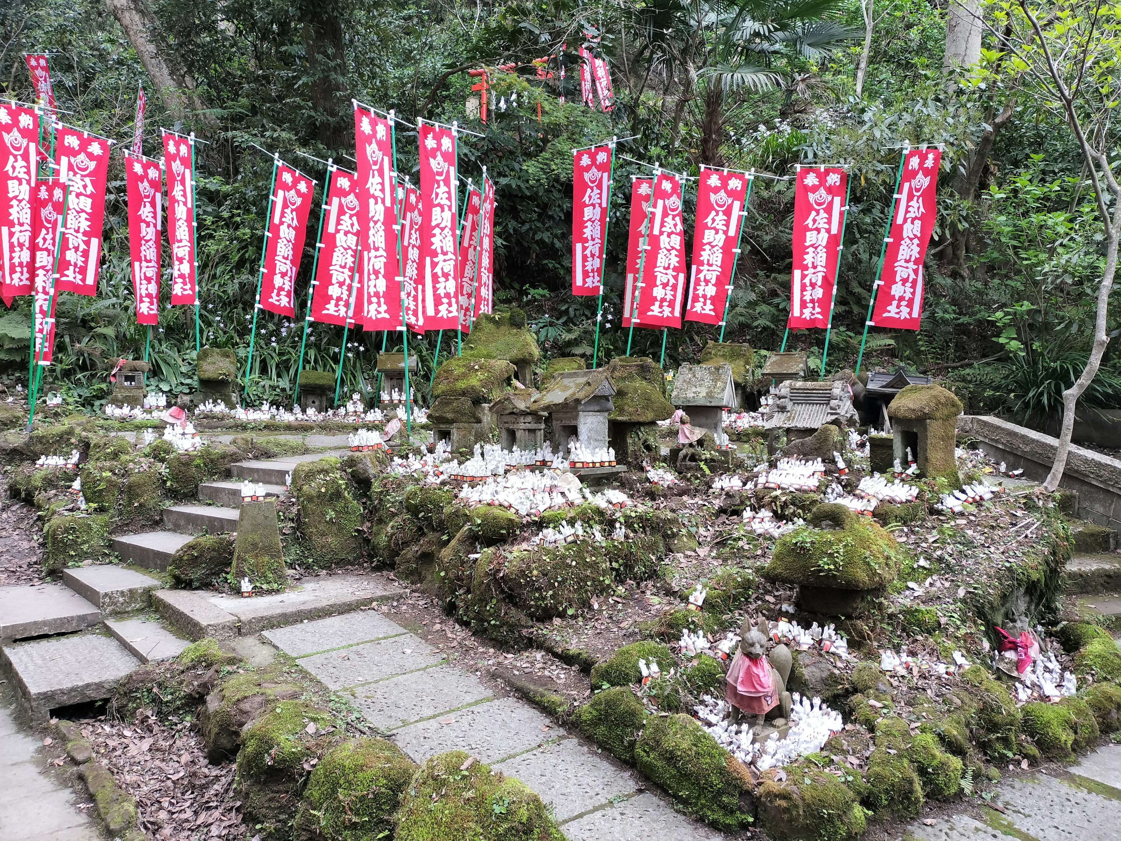 石段と苔の生えた庭に赤い旗が立っている神社の風景