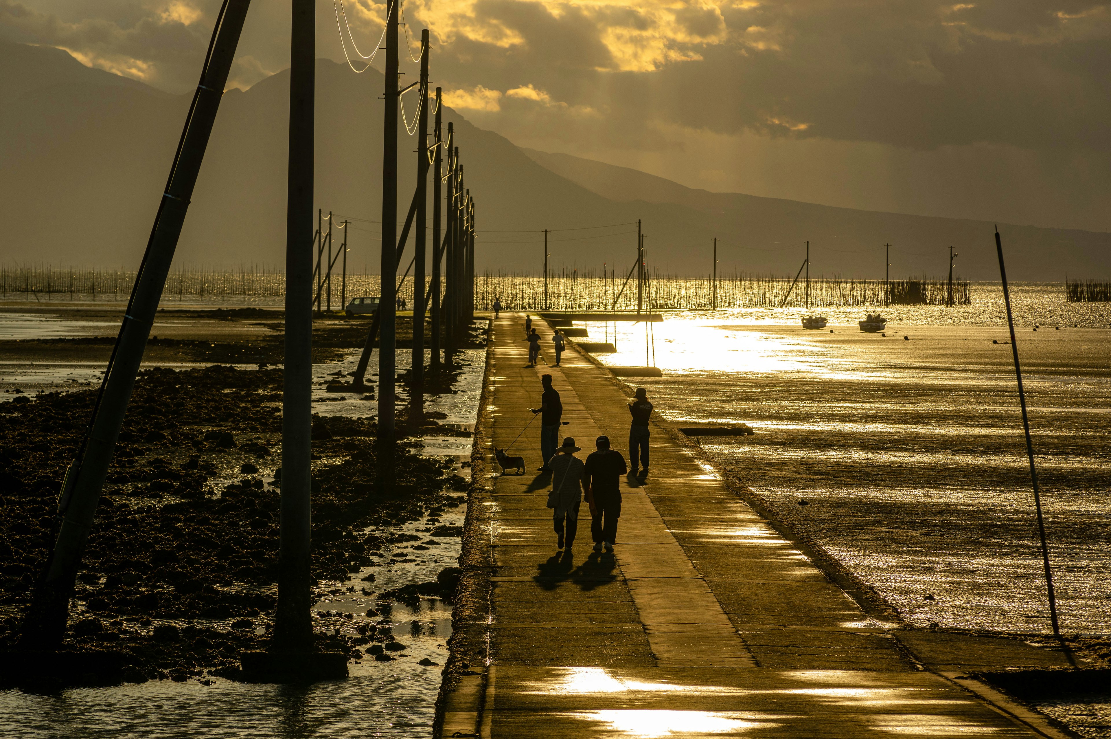 People walking along a coastal pier at sunset with a shimmering water surface