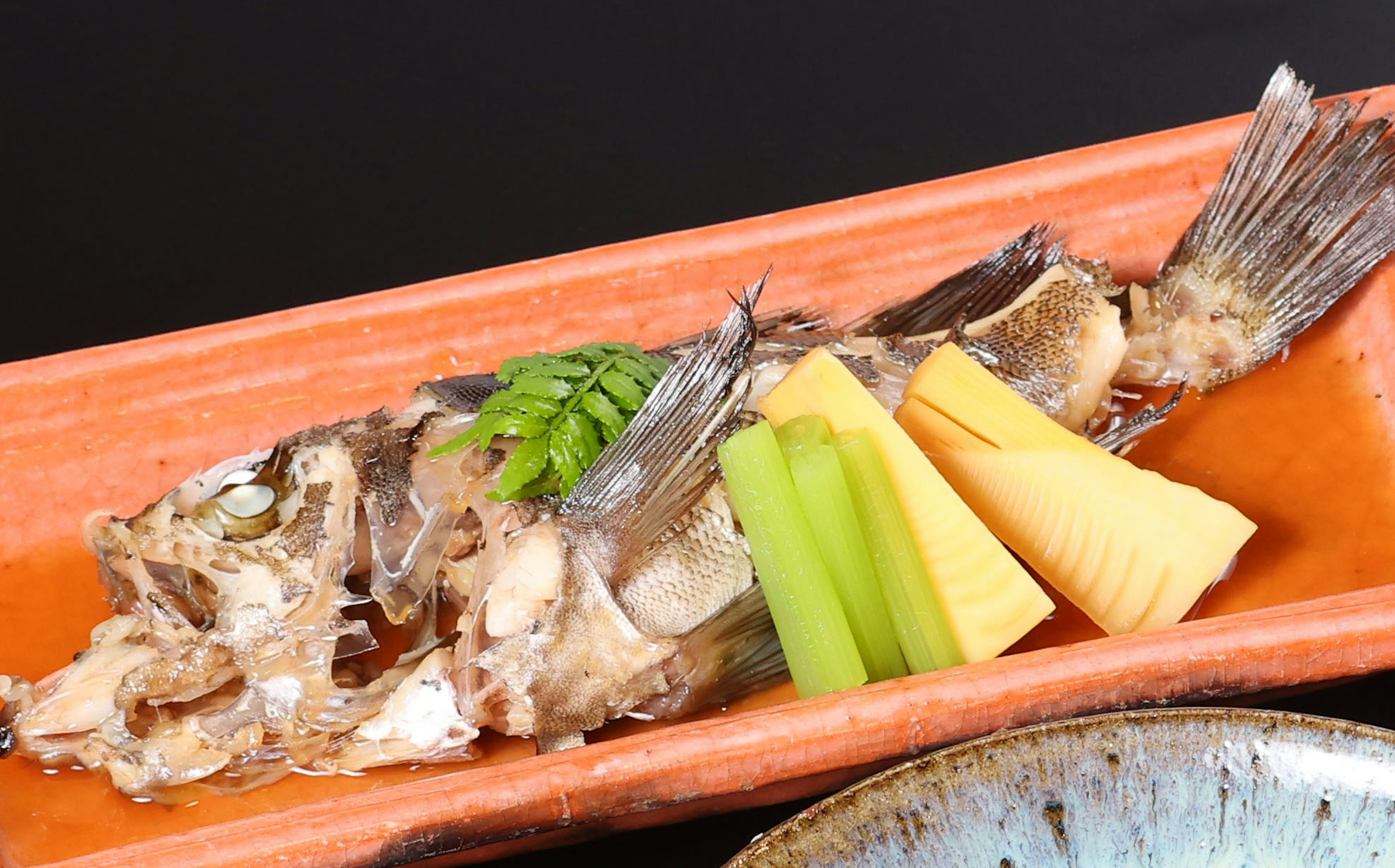 Pescado a la parrilla servido en un plato naranja con espárragos y brotes de bambú