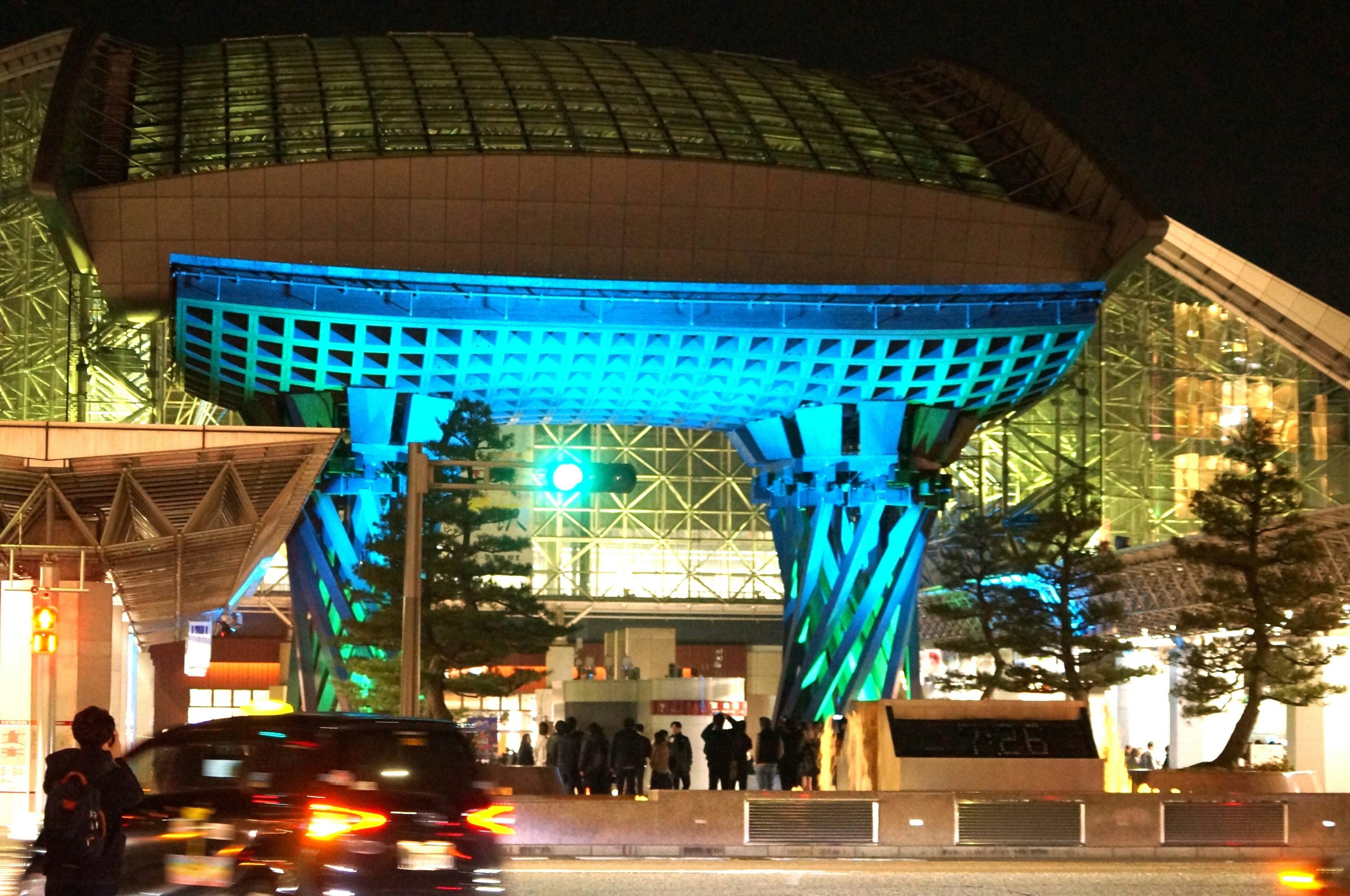 Entrada iluminada de un edificio por la noche con una gran estructura azul y fachada de vidrio