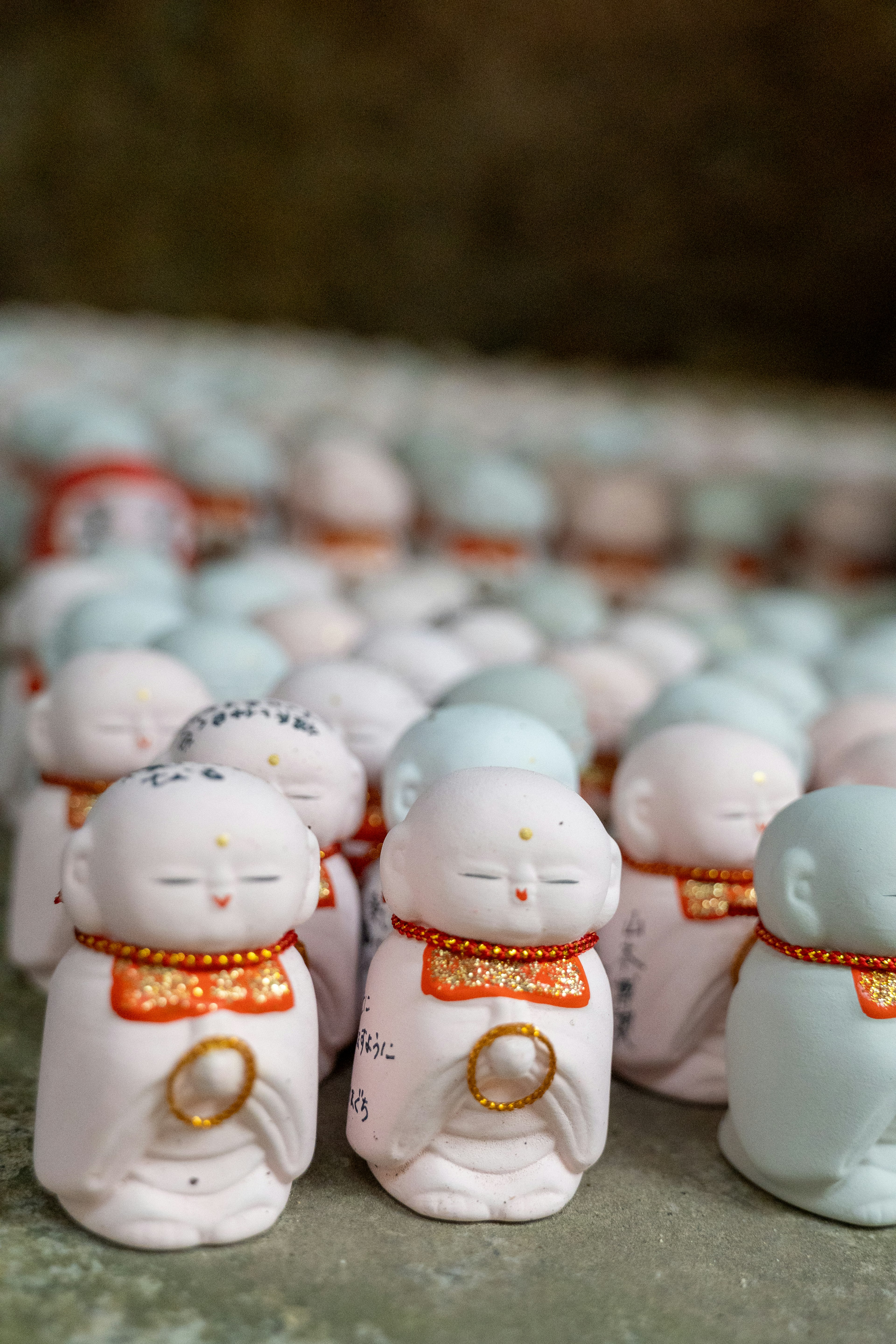 A row of small ceramic Buddha statues with distinctive red sashes