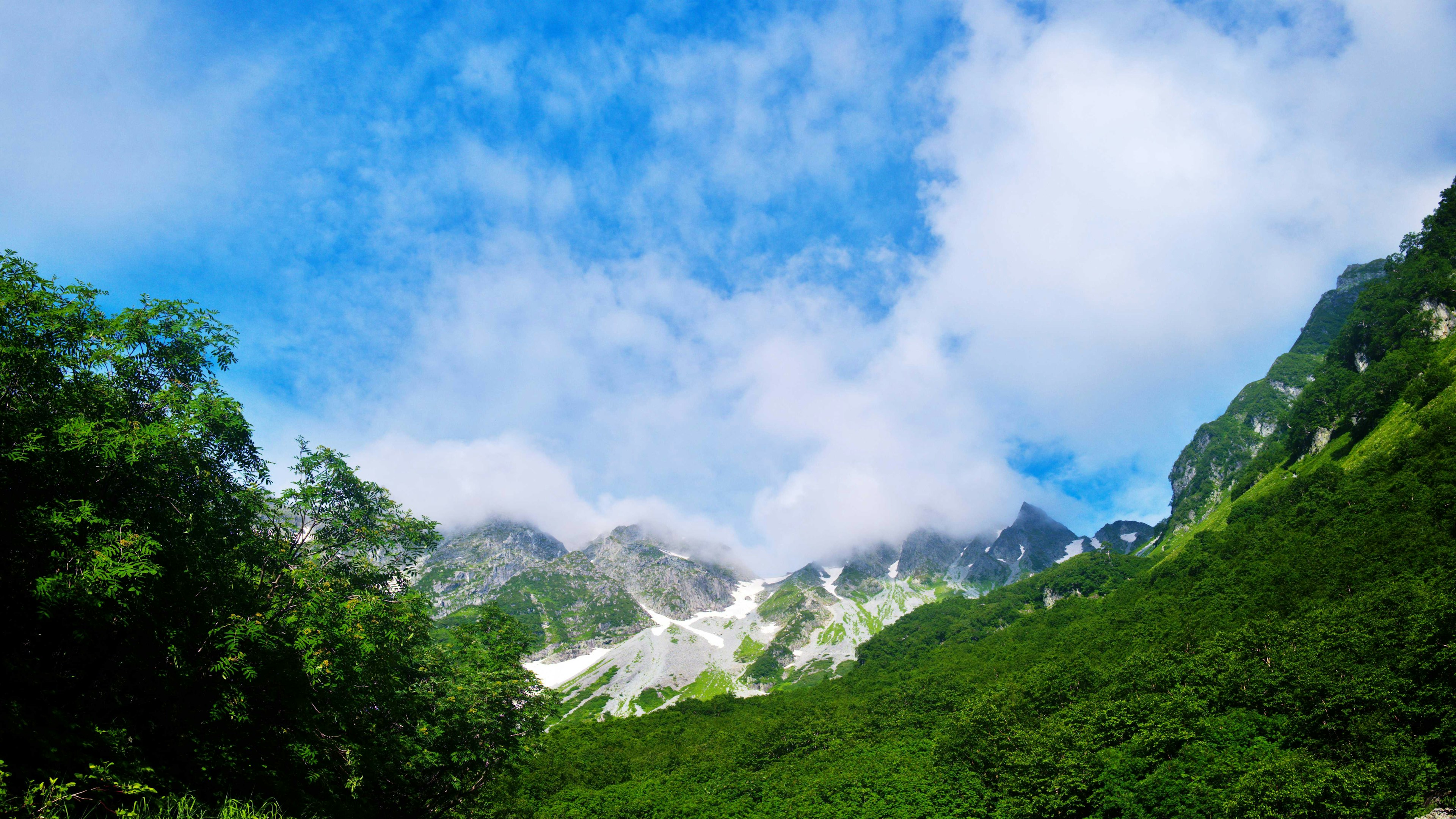 Gunung hijau subur di bawah langit biru dengan awan putih