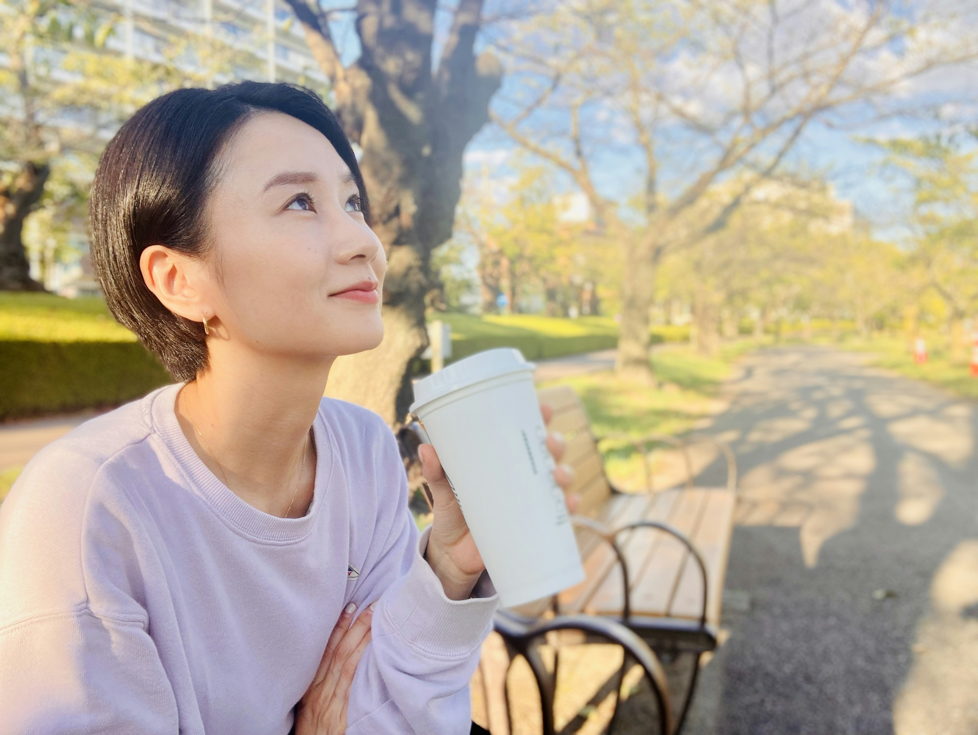 Mujer sosteniendo una taza de café mientras contempla en un parque