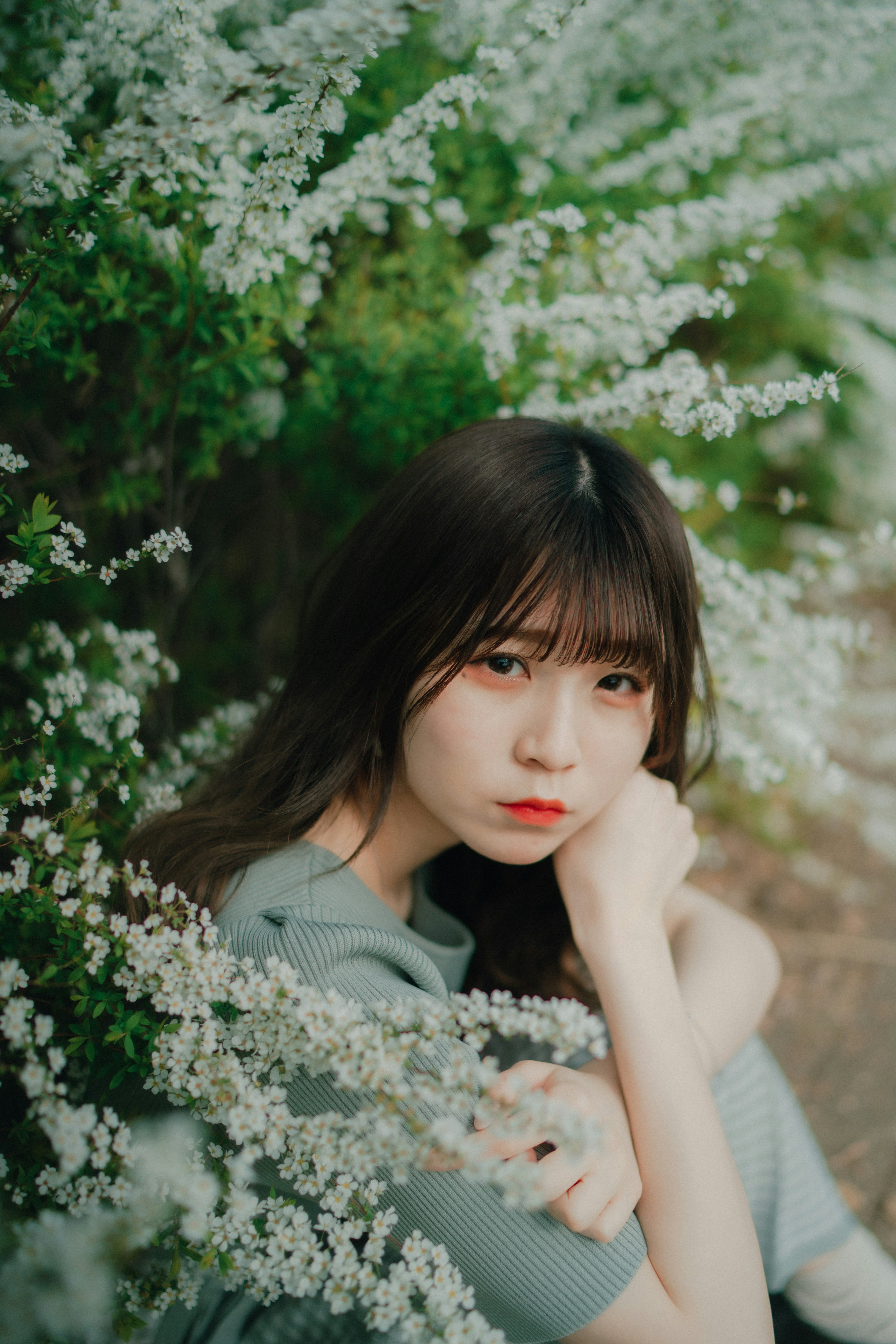 A girl resting her chin on her hand surrounded by white flowers