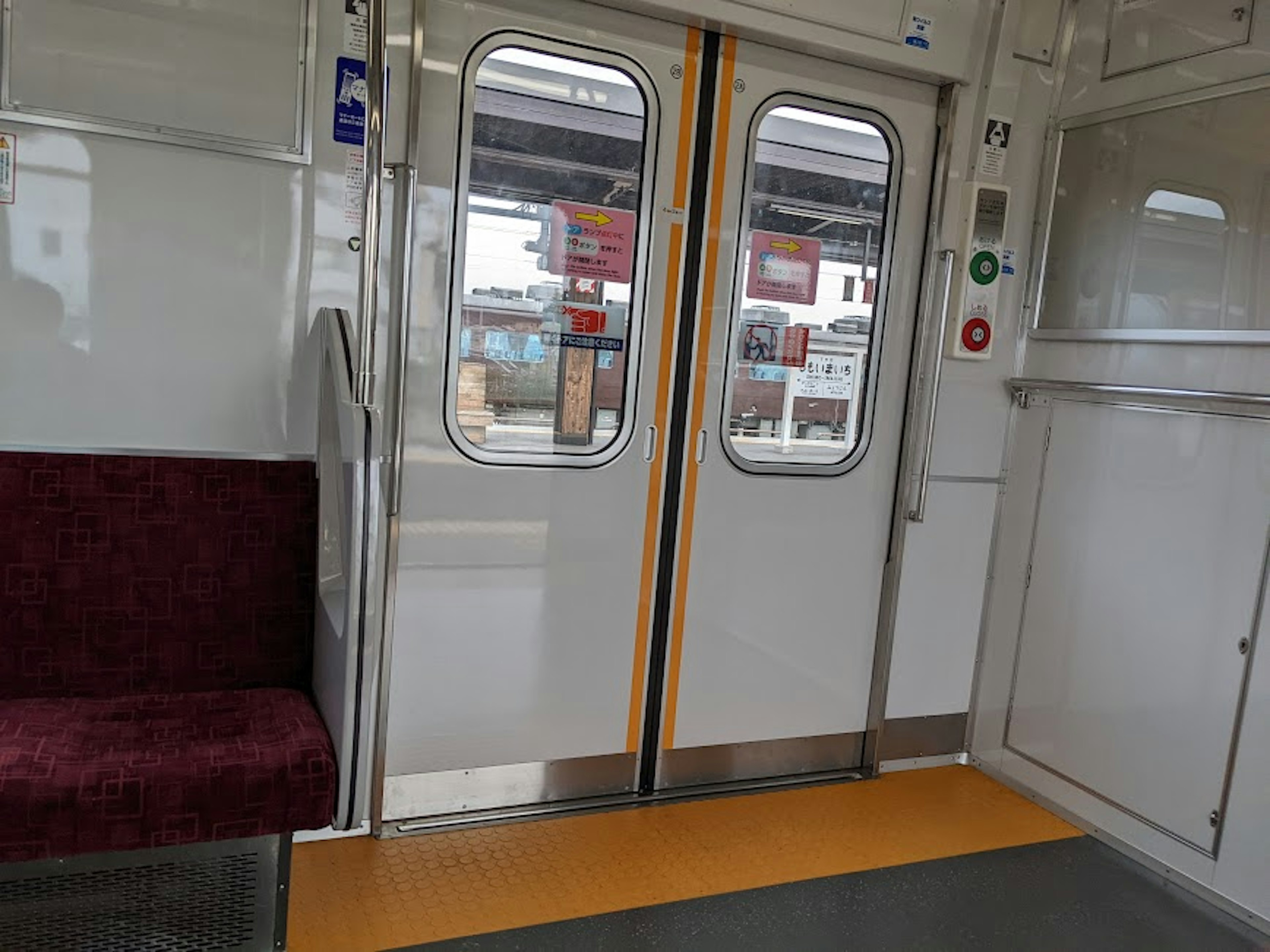 Interior of an empty train compartment with doors and a red seat