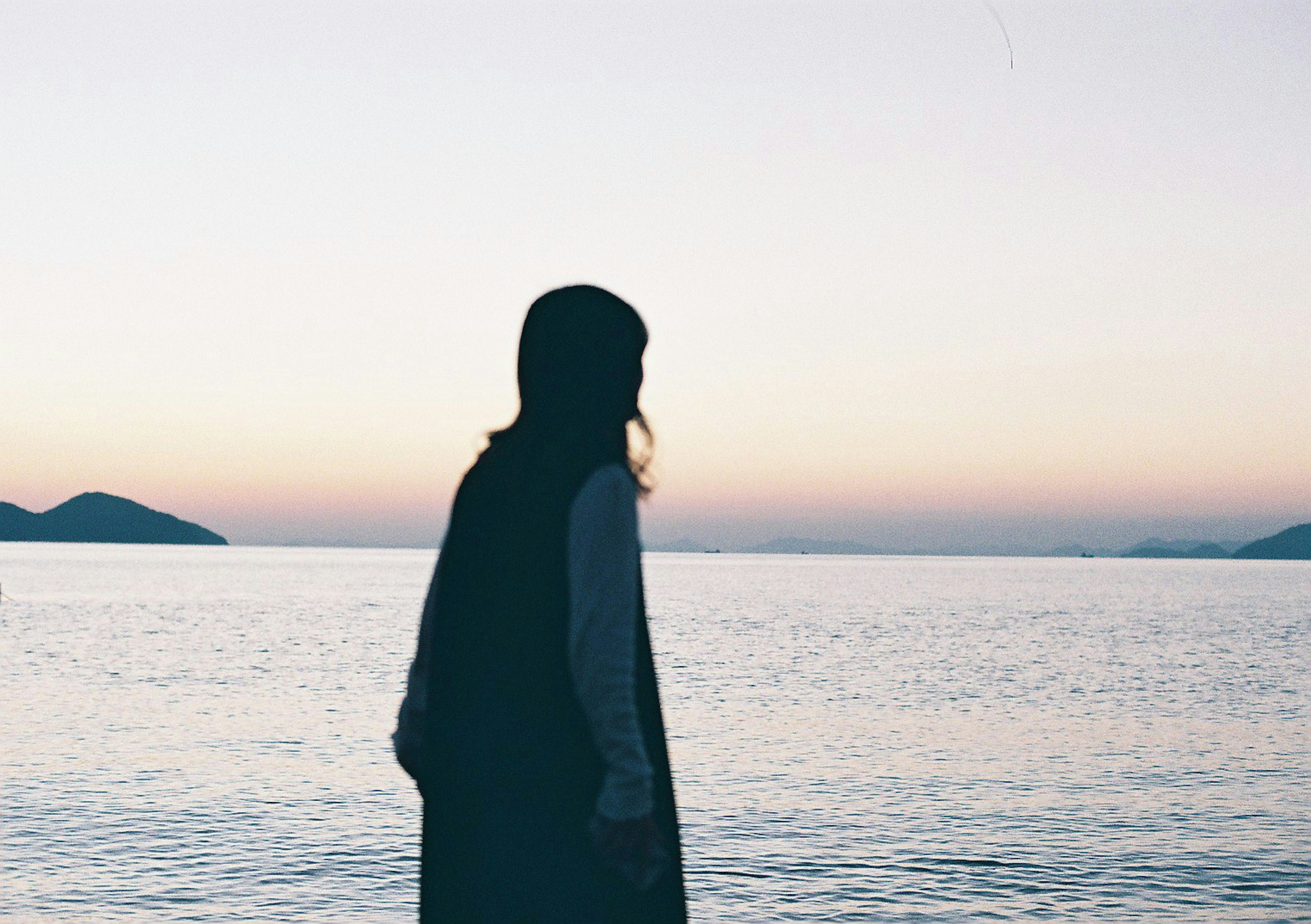 Silhouette wanita menatap laut dengan langit senja yang tenang