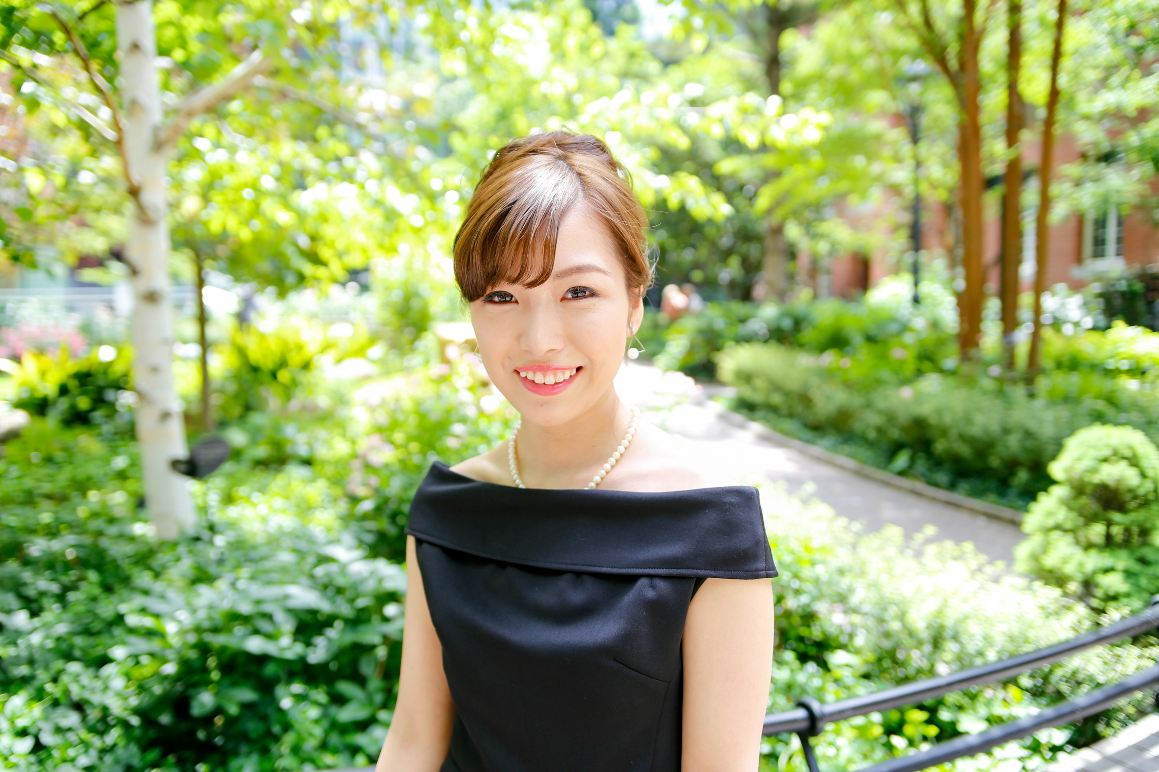 Retrato de una mujer sonriendo en un parque verde con un vestido negro y el cabello recogido