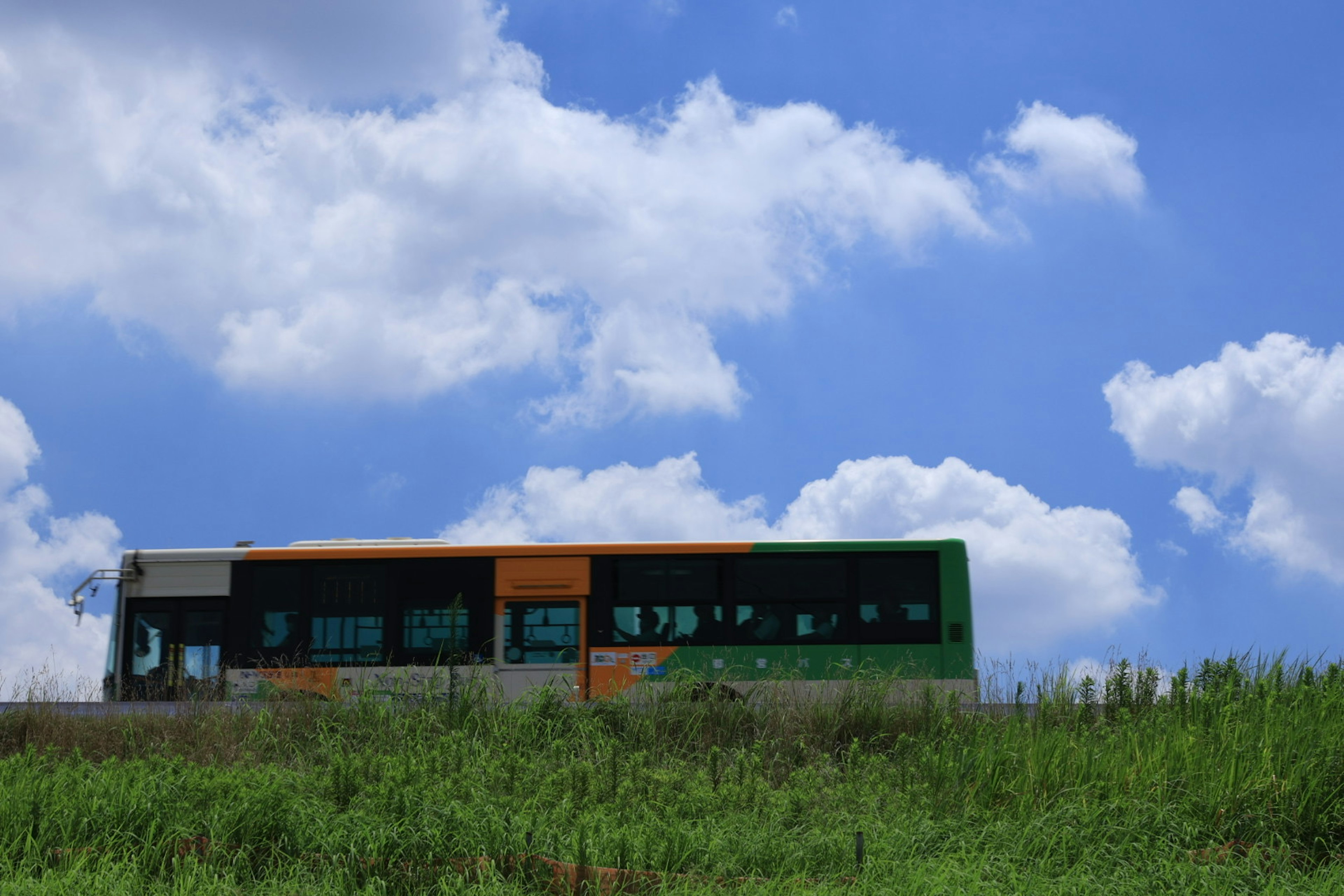 Bus in Orange und Grün vor blauem Himmel und grasigem Feld