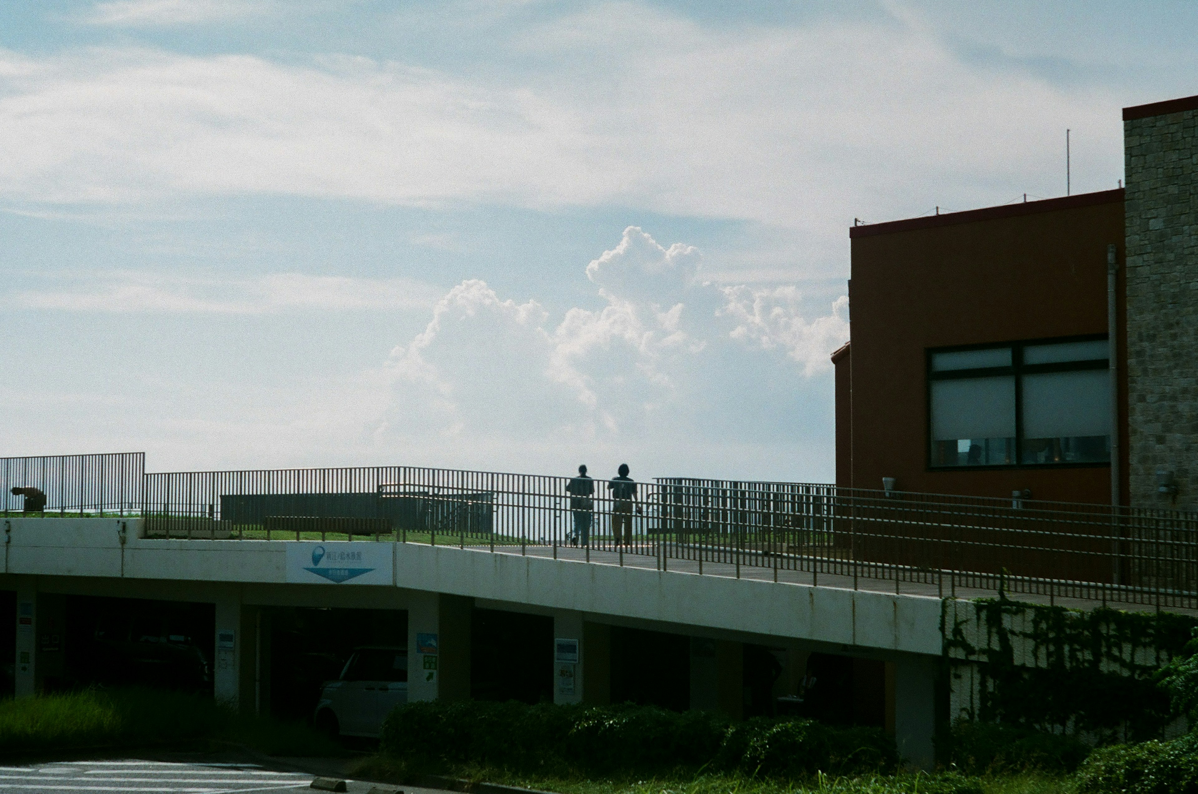 青空と雲の下で立つ二人の人物と建物の外観