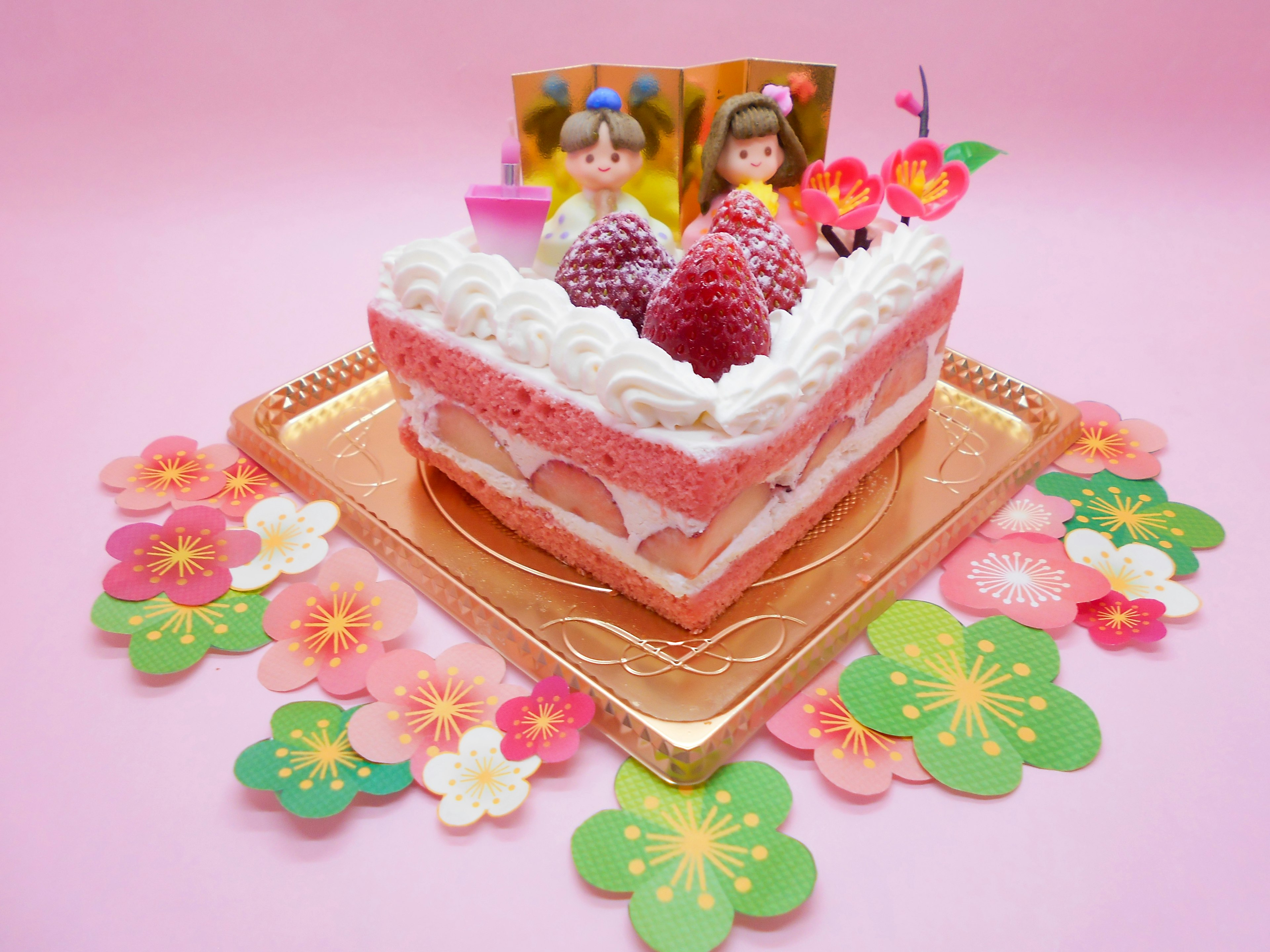 Cute decorated cake on a pink background with fruits and cream on a square cake featuring small dolls and flower decorations